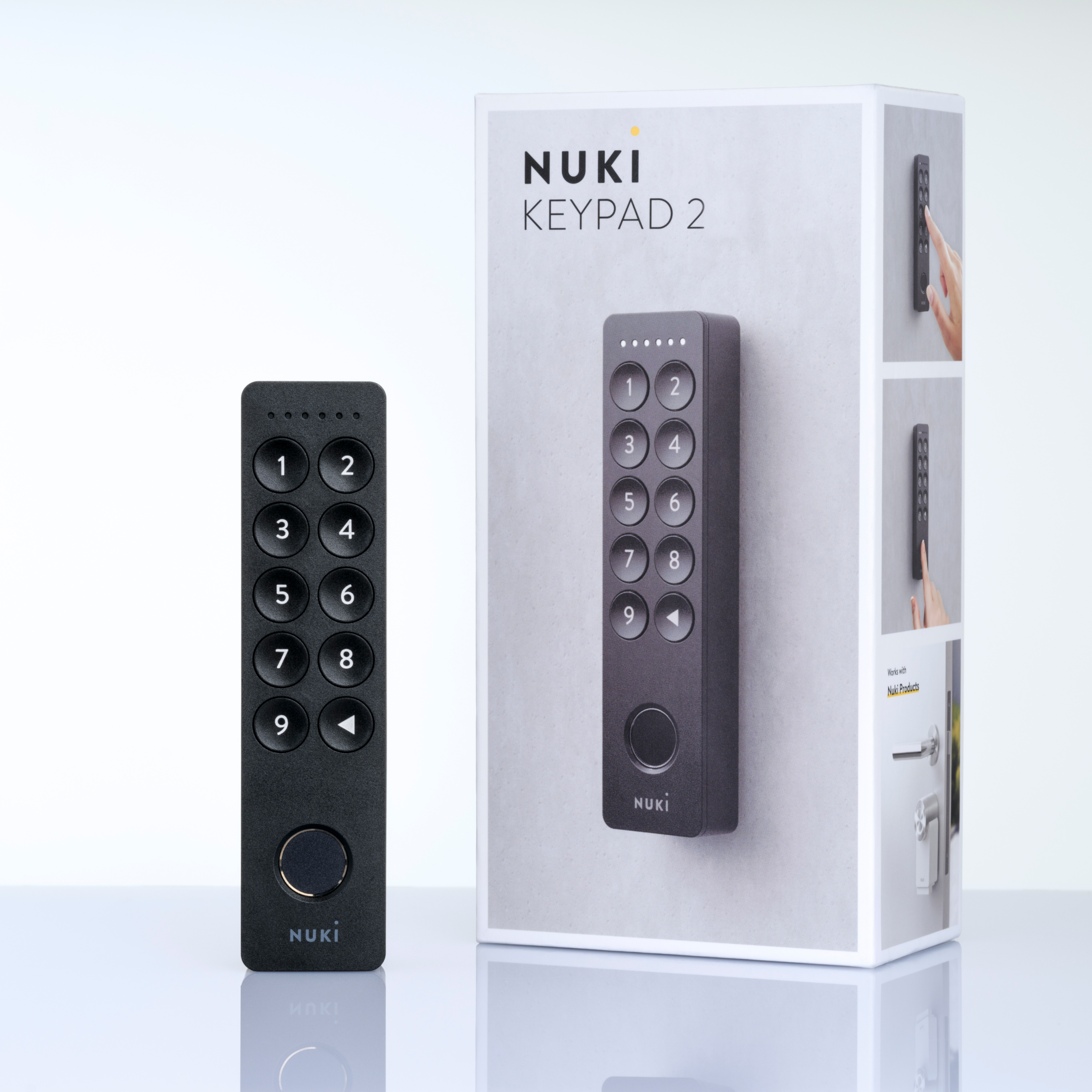 Nuki Keypad 2 in Schwarz steht links vor der Originalverpackung auf heller Oberfläche.
