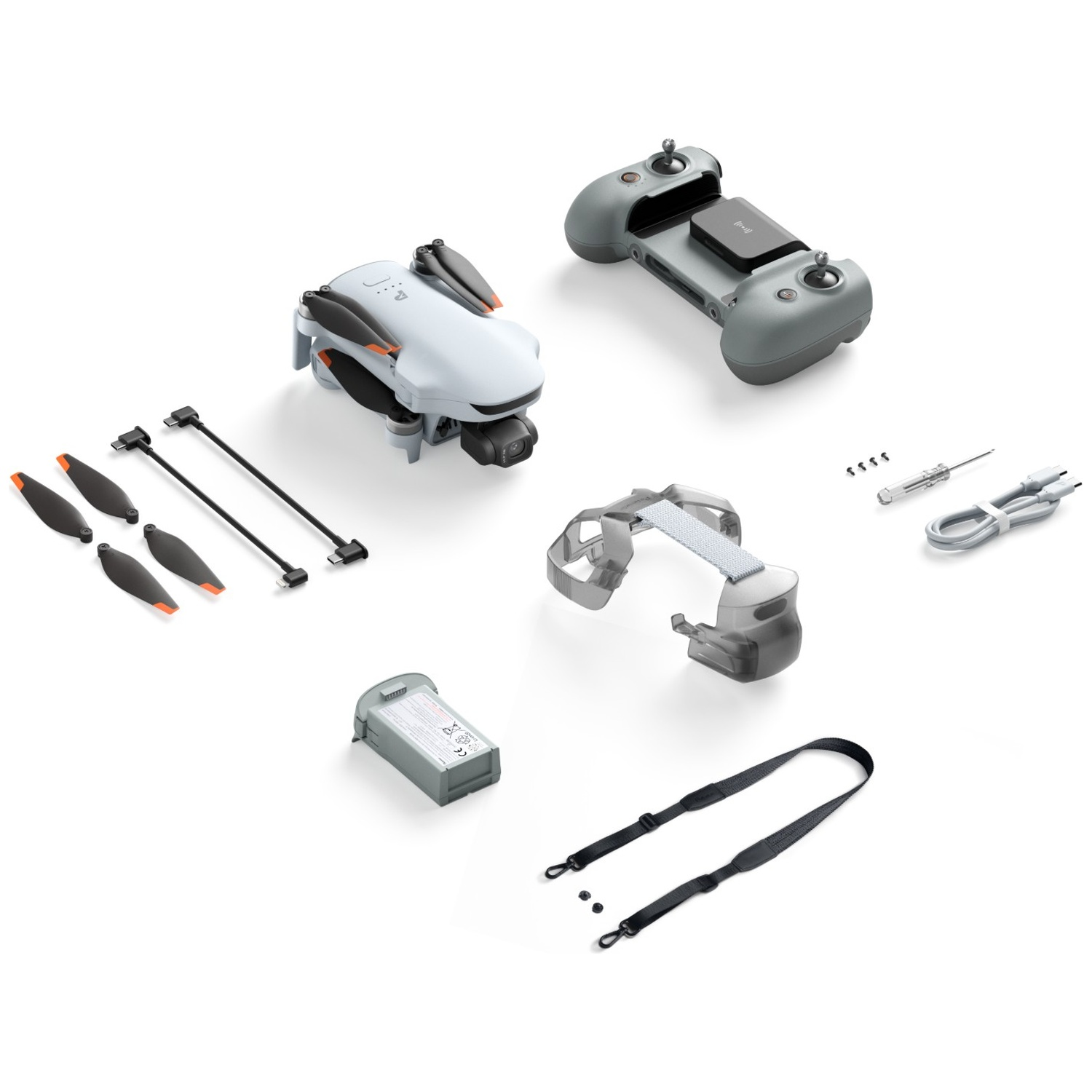Drone gris avec télécommande, batterie, hélices de rechange, câbles et accessoires sur fond blanc.