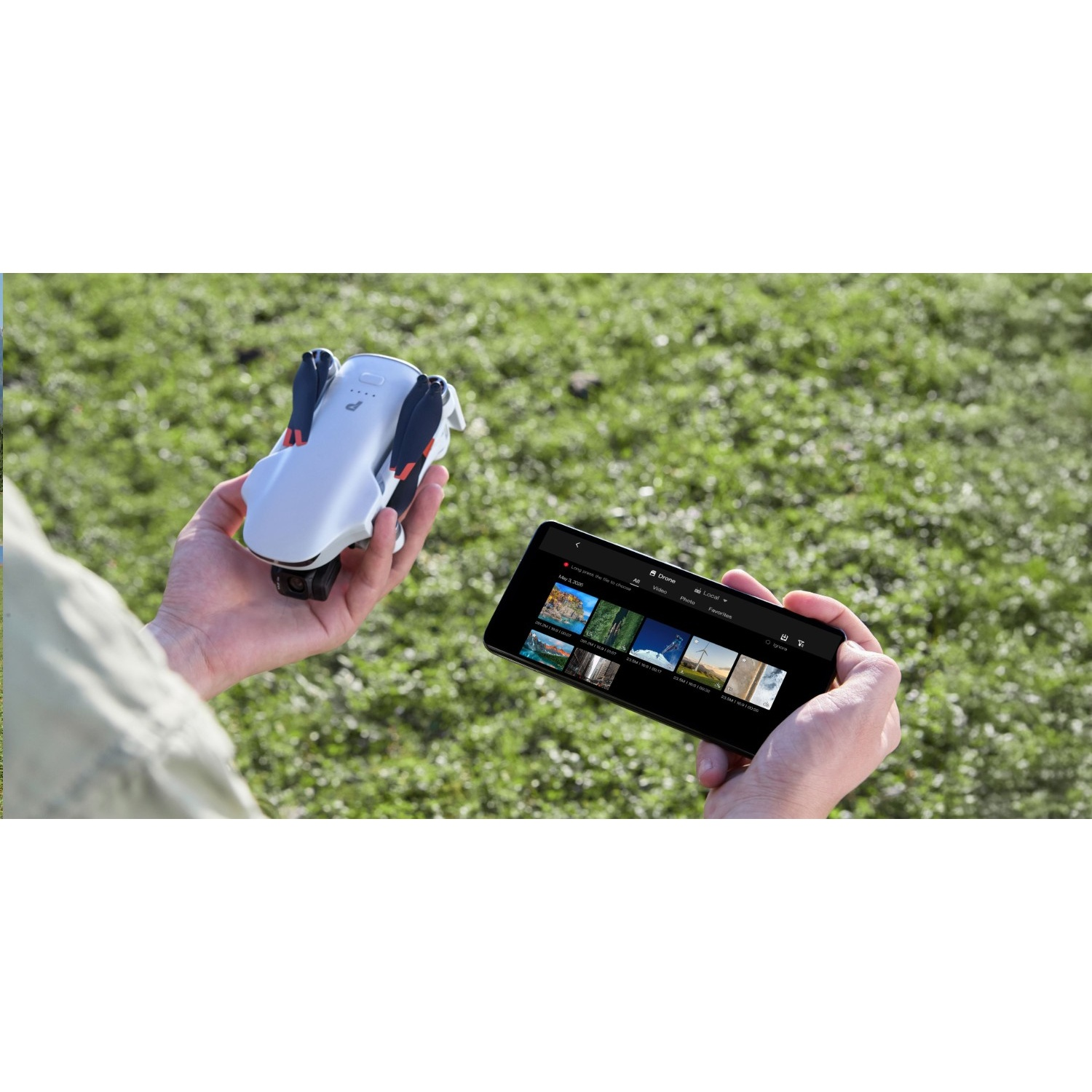 Une personne tient un drone blanc d'une main et un smartphone affichant une galerie de photos de l'autre, sur de l'herbe.