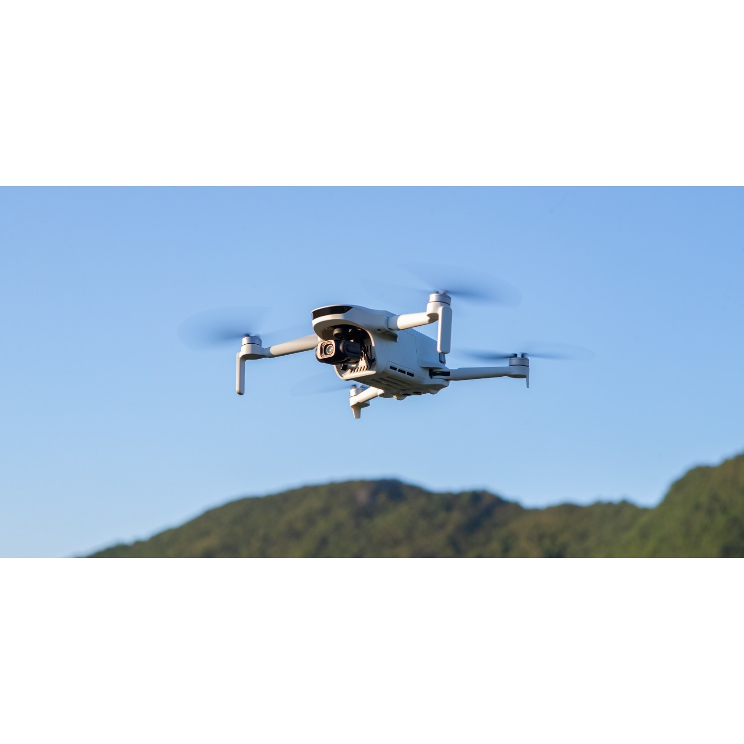 Un drone blanc vole dans un ciel bleu au-dessus de collines vertes.