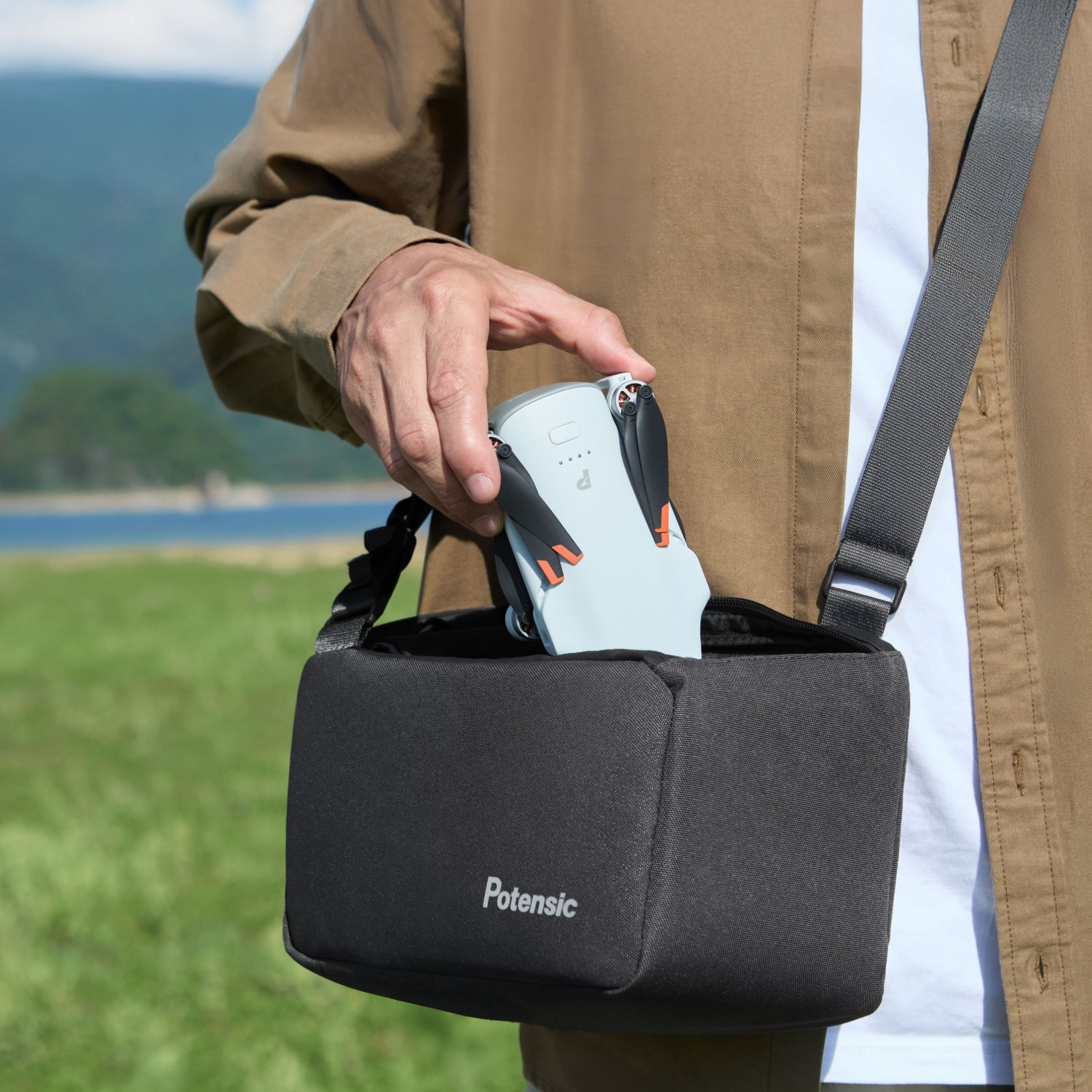 Personne rangeant un drone compact dans un sac bandoulière noir Potensic, nature en arrière-plan.