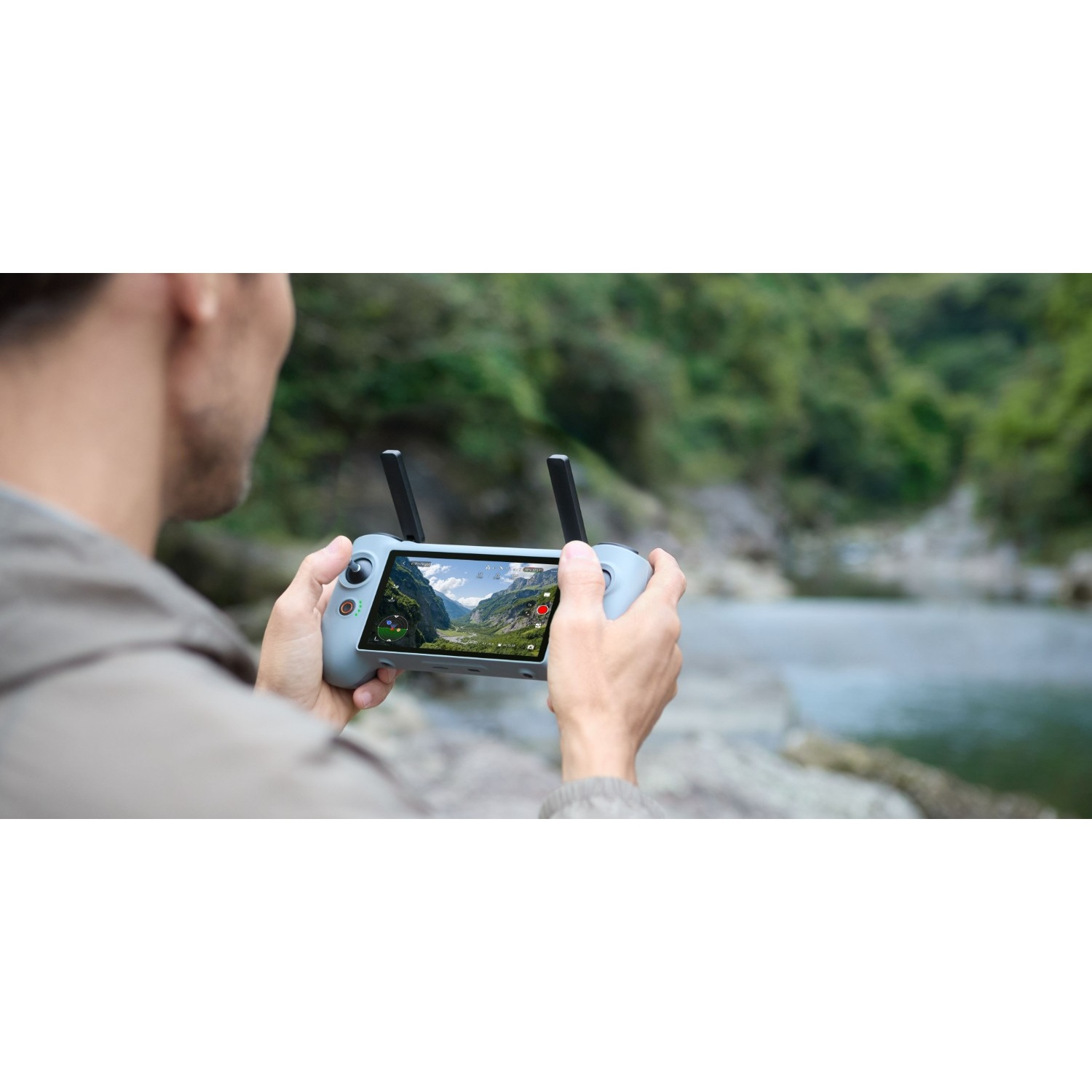 Une personne tient une radiocommande de drone grise affichant un paysage de montagne vert sur son écran.