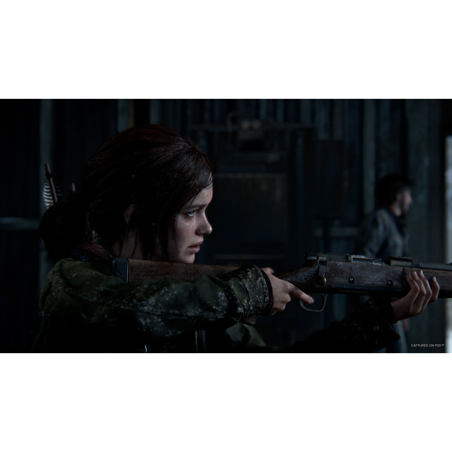 Une femme concentrée vise avec un fusil dans une pièce sombre, avec une autre personne debout en arrière-plan.