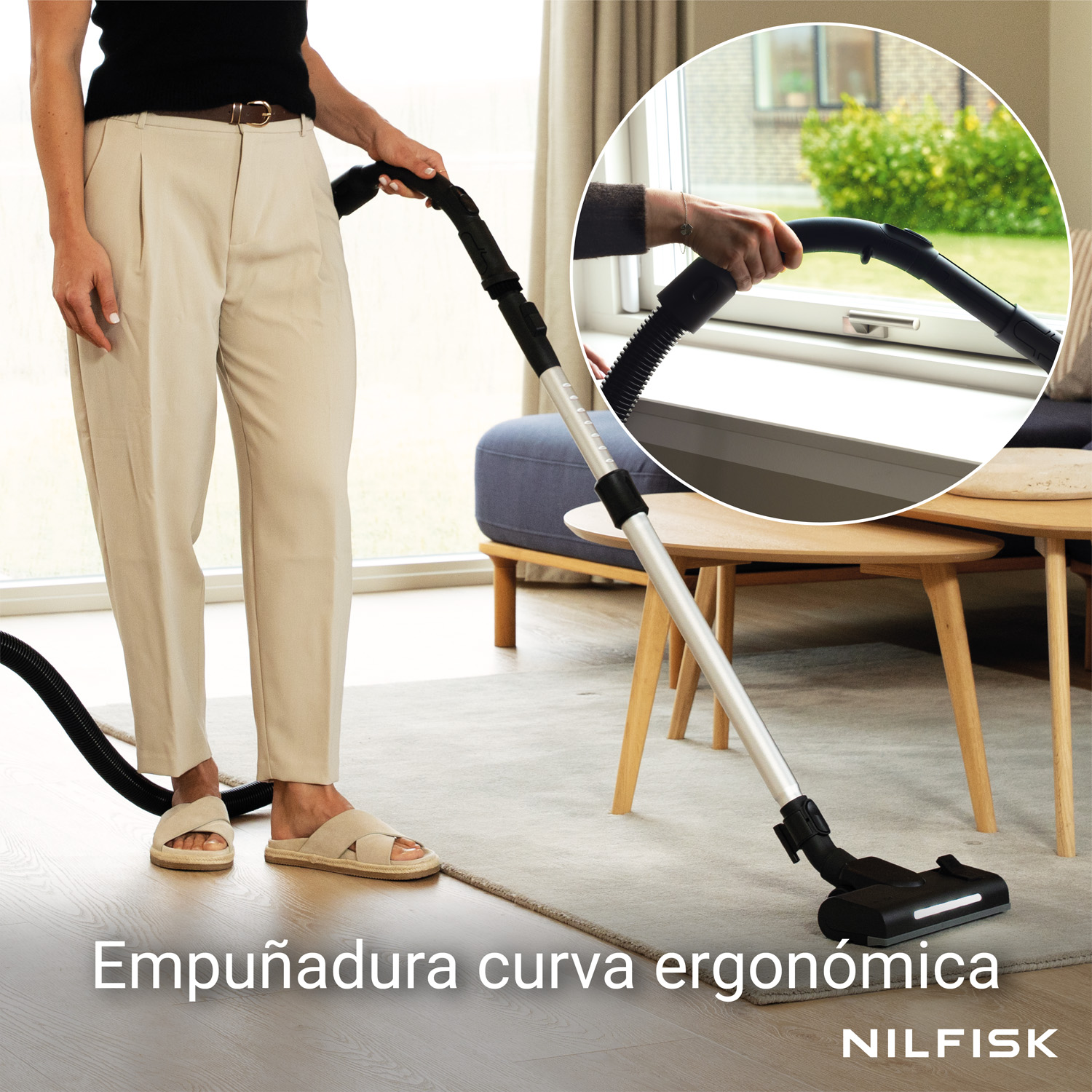 Persona pasando la aspiradora con empuñadura ergonómica sobre una alfombra en una habitación luminosa.