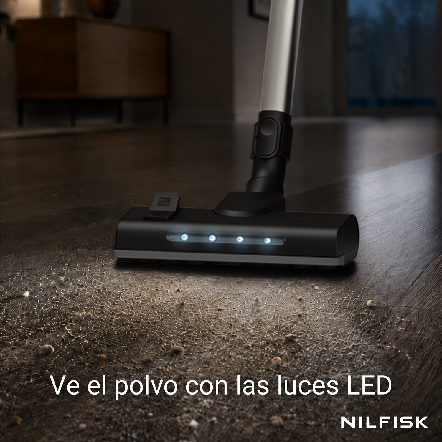 Una aspiradora con luces LED ilumina la suciedad en un suelo de madera oscura en una habitación.