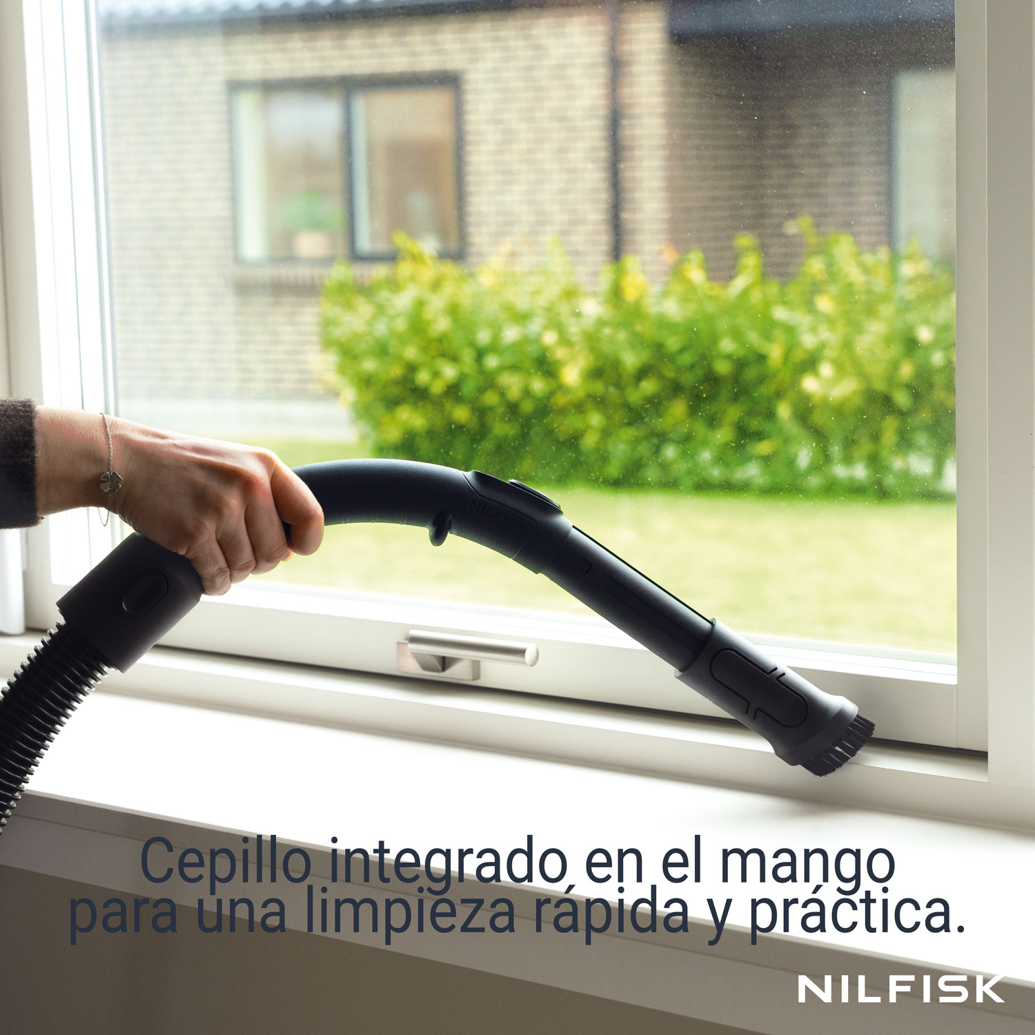 Una mano sostiene el mango negro de una aspiradora junto a una ventana blanca con texto abajo.