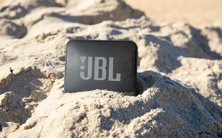 Kumlu bir plajda duran siyah bir JBL hoparlör.