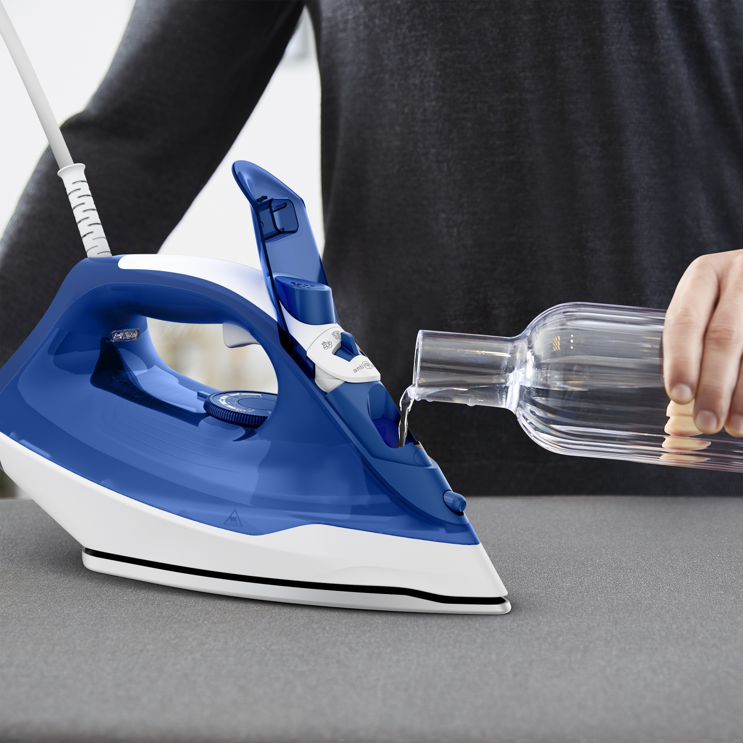 A person pours water from a bottle into a blue and white steam iron.