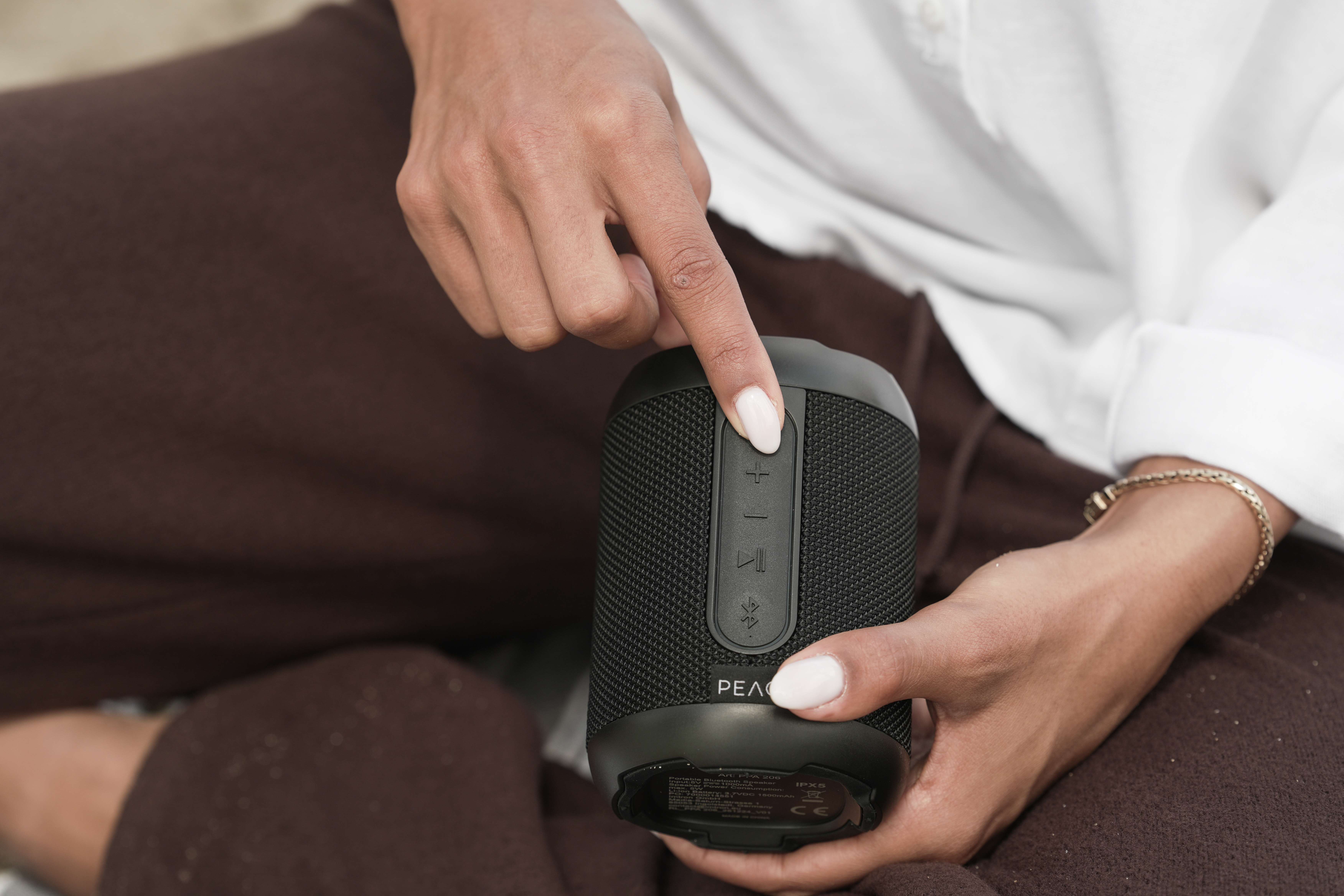 Osoba naciska przycisk głośności na małym czarnym głośniku Bluetooth.