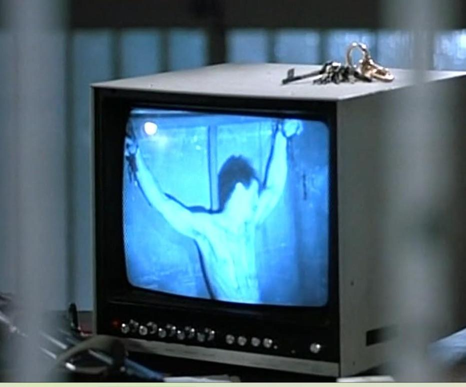 Ein alter Fernseher zeigt einen gefesselten Mann in Blau, Schlüssel liegen oben auf.