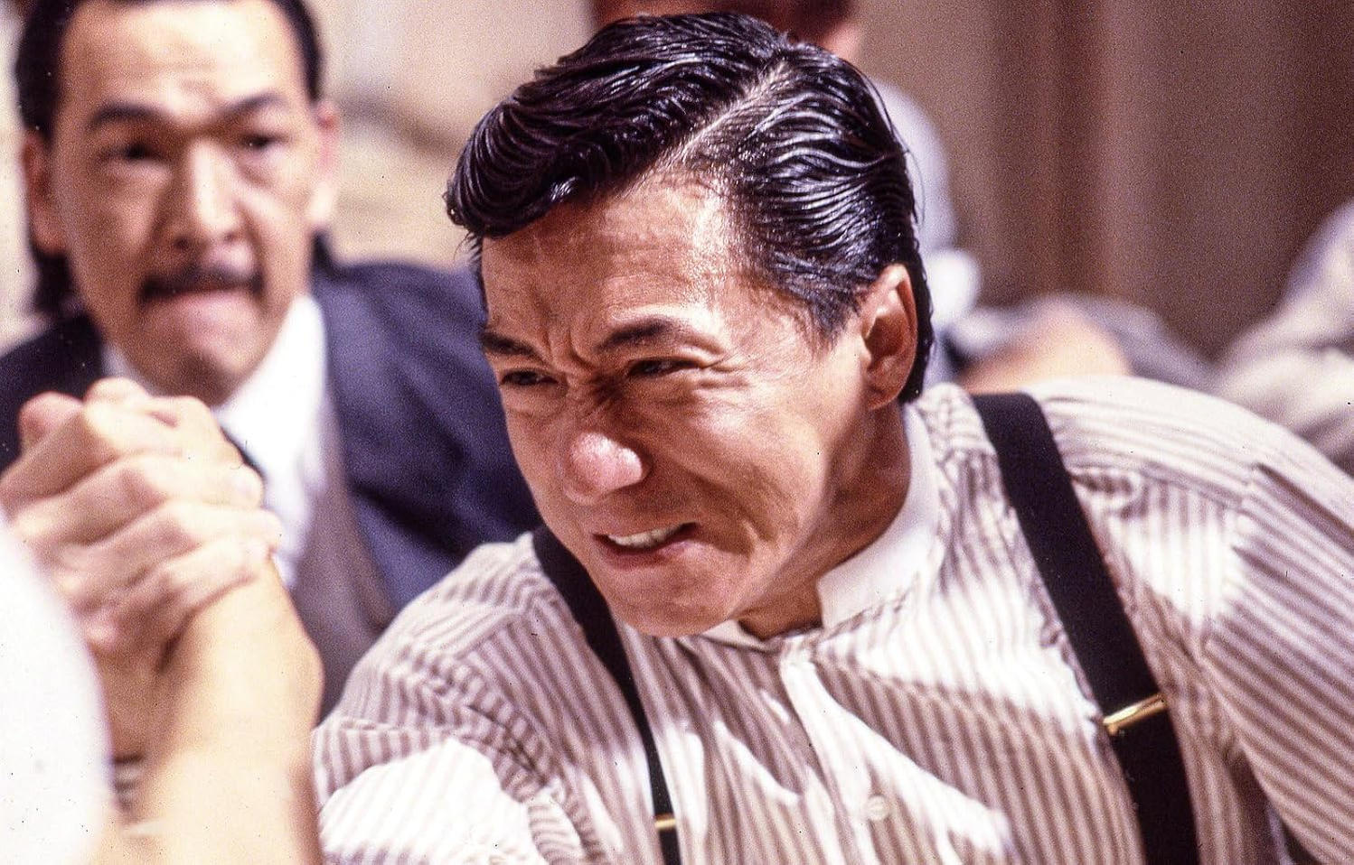 Jackie Chan konzentriert sich beim Armdrücken in einem Raum.