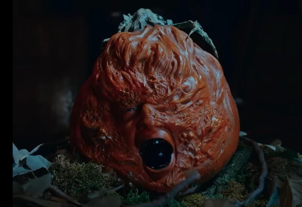 Eine gruselige Kürbisskulptur mit einem menschlichen Gesicht, das in einem dunklen Raum den Mund öffnet.
