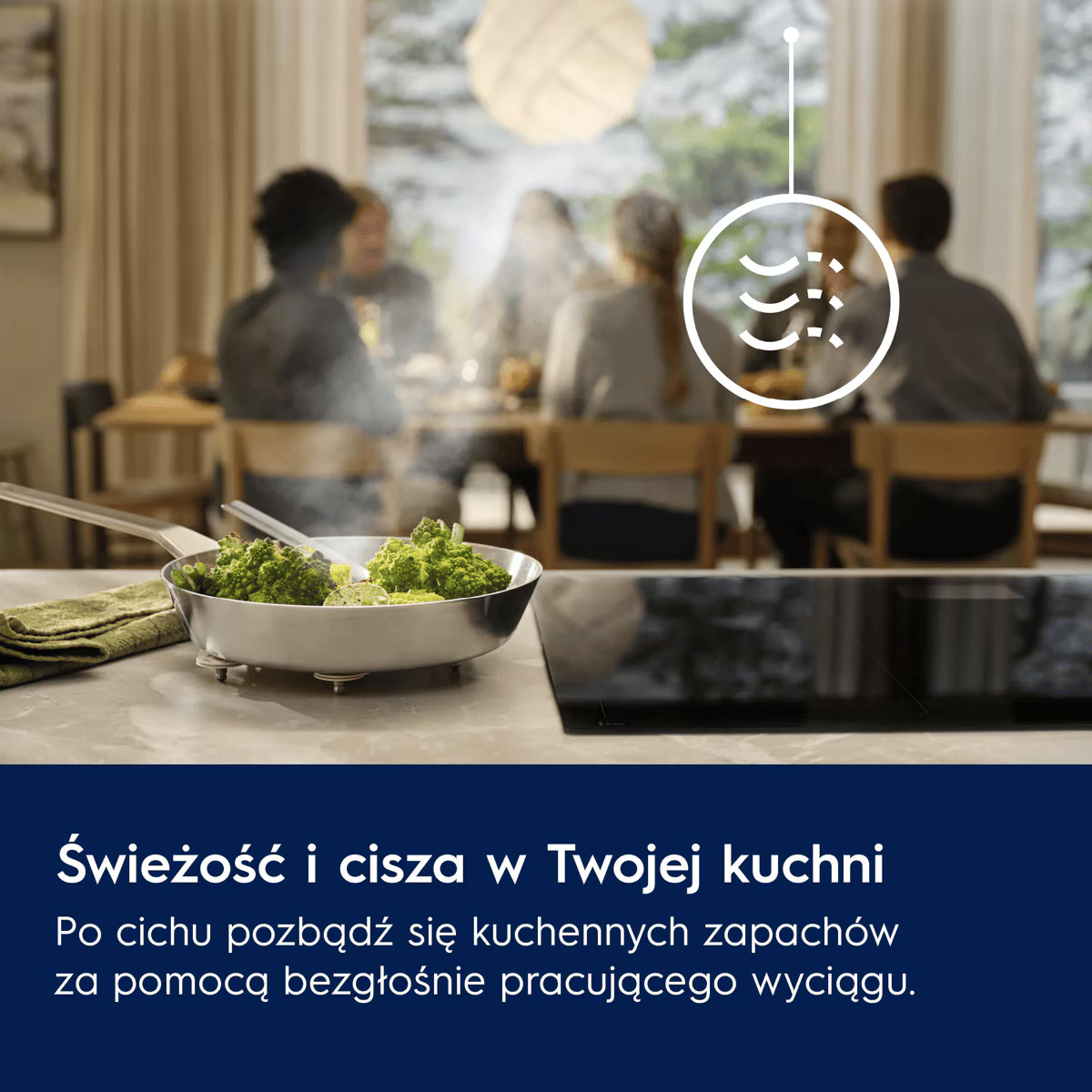 Patelnia z parującymi warzywami na blacie, w tle rozmyte osoby jedzące posiłek przy stole.