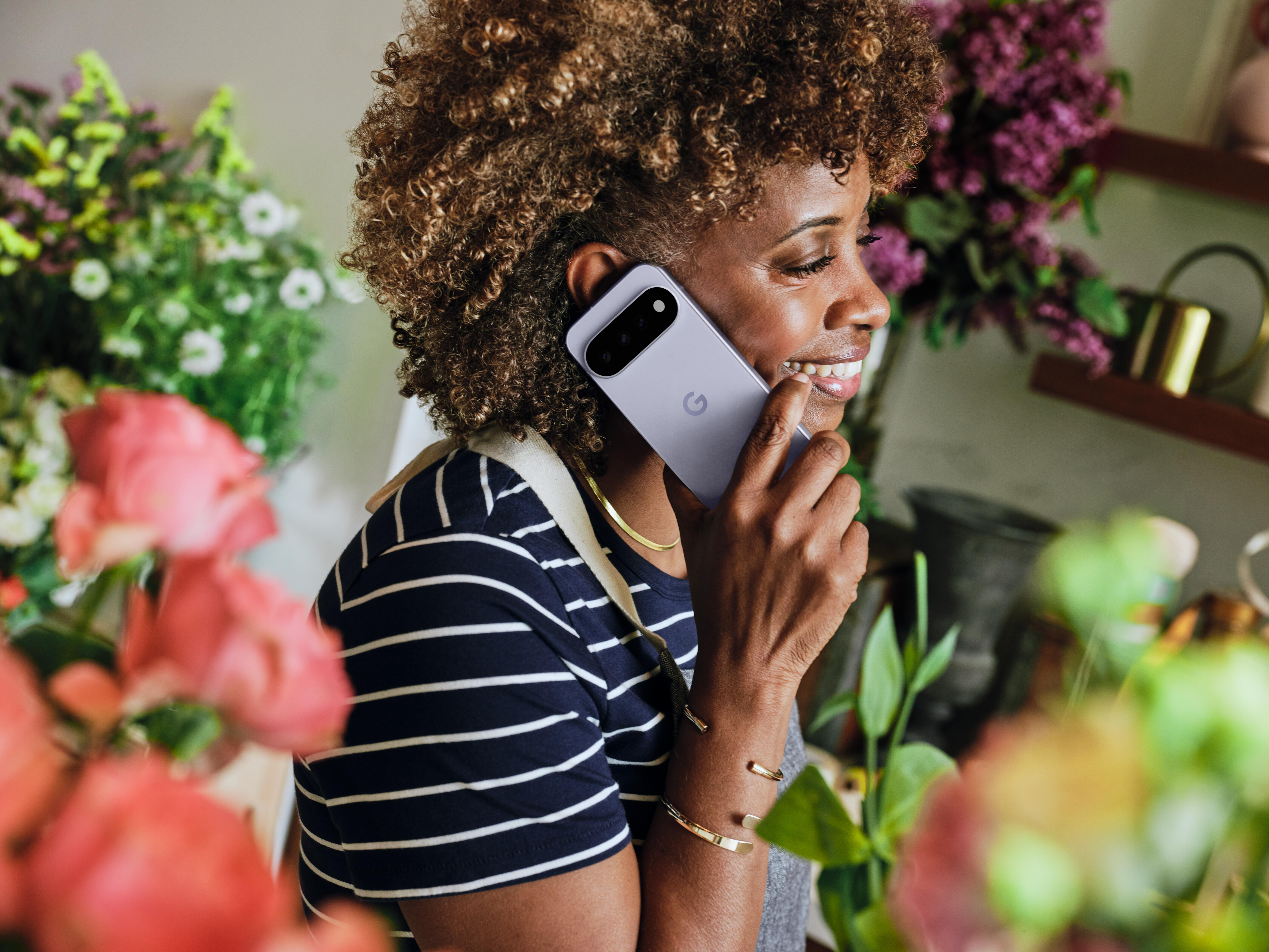 Eine Frau mit Locken lächelt und telefoniert in einem Blumenladen.