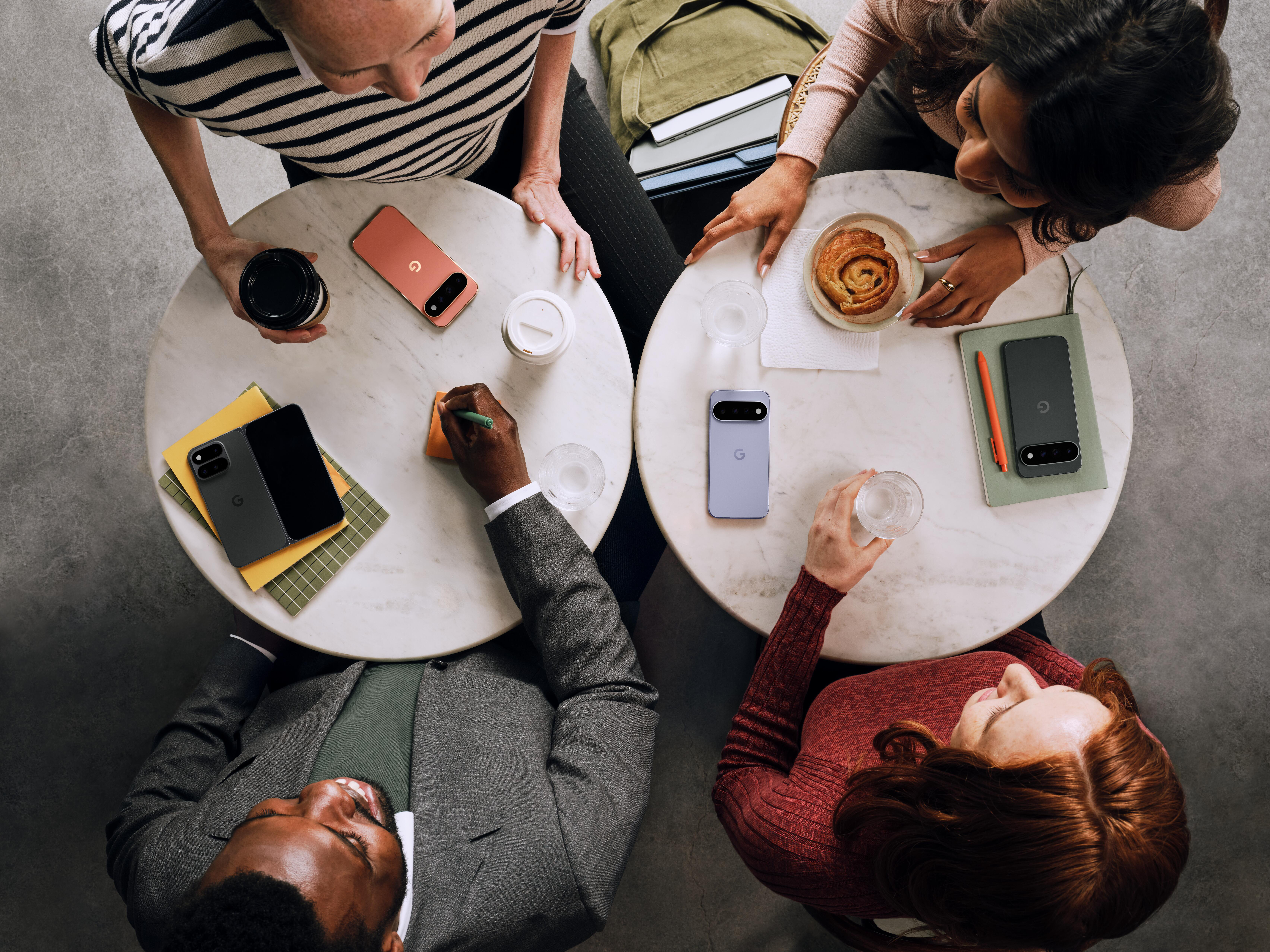 Vier Personen sitzen an runden Tischen, umgeben von Smartphones, Notizbüchern, Kaffee und Gebäck.