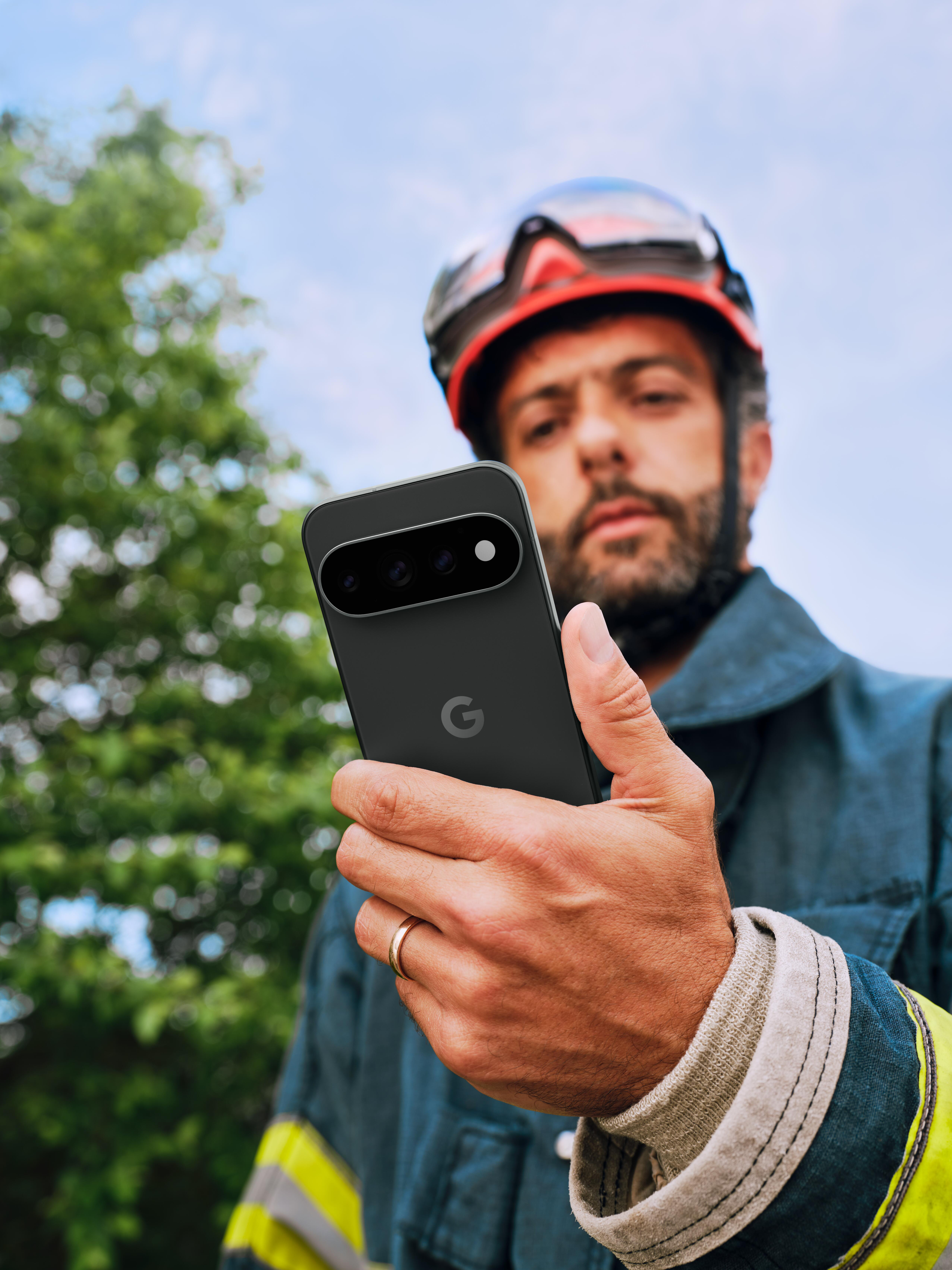 Feuerwehrmann mit Helm hält ein schwarzes Google-Smartphone mit sichtbarer Rückkamera und Logo.