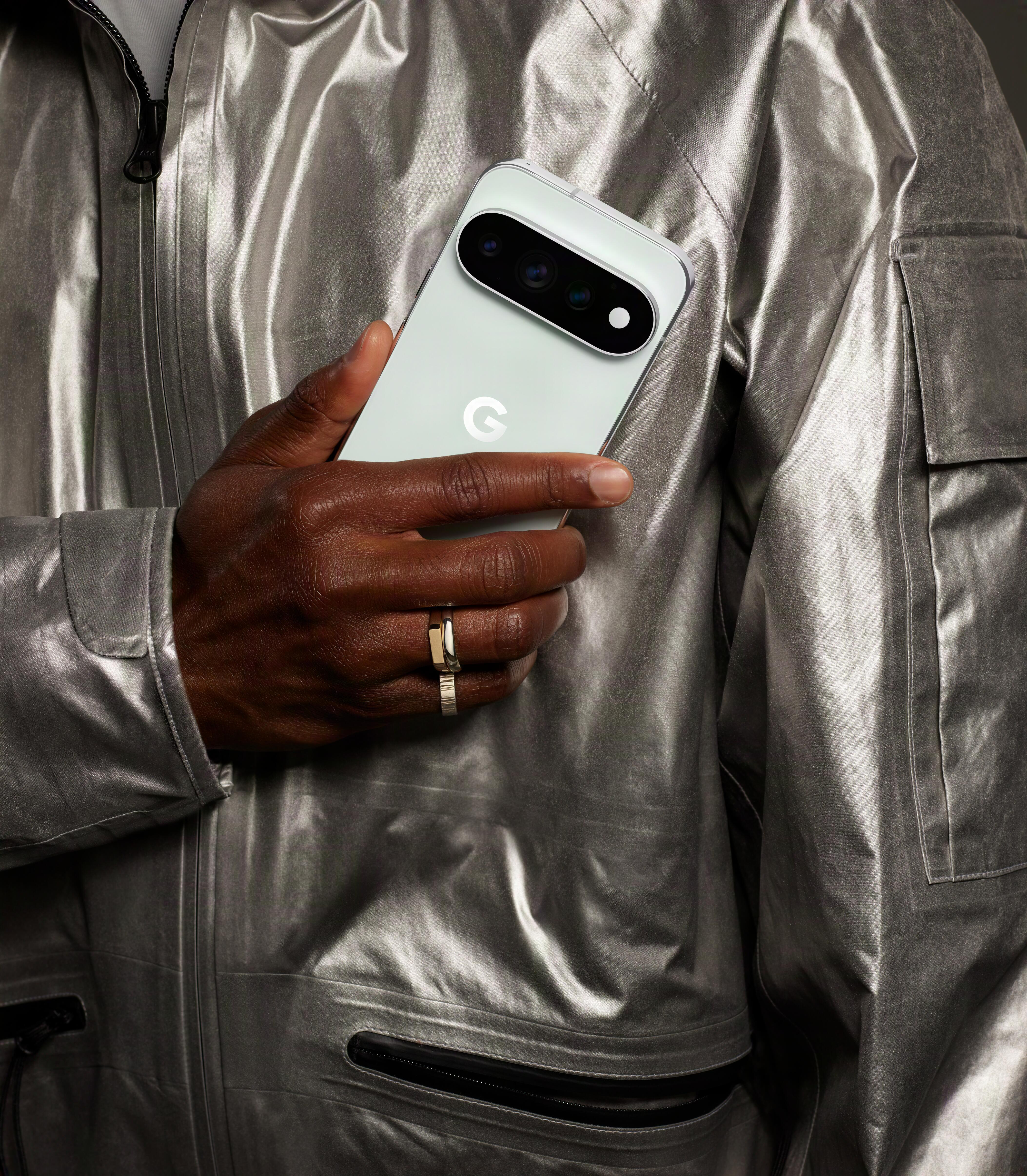 Eine Person in einer silbernen Jacke hält ein hellgrünes Smartphone mit einer Kamera.