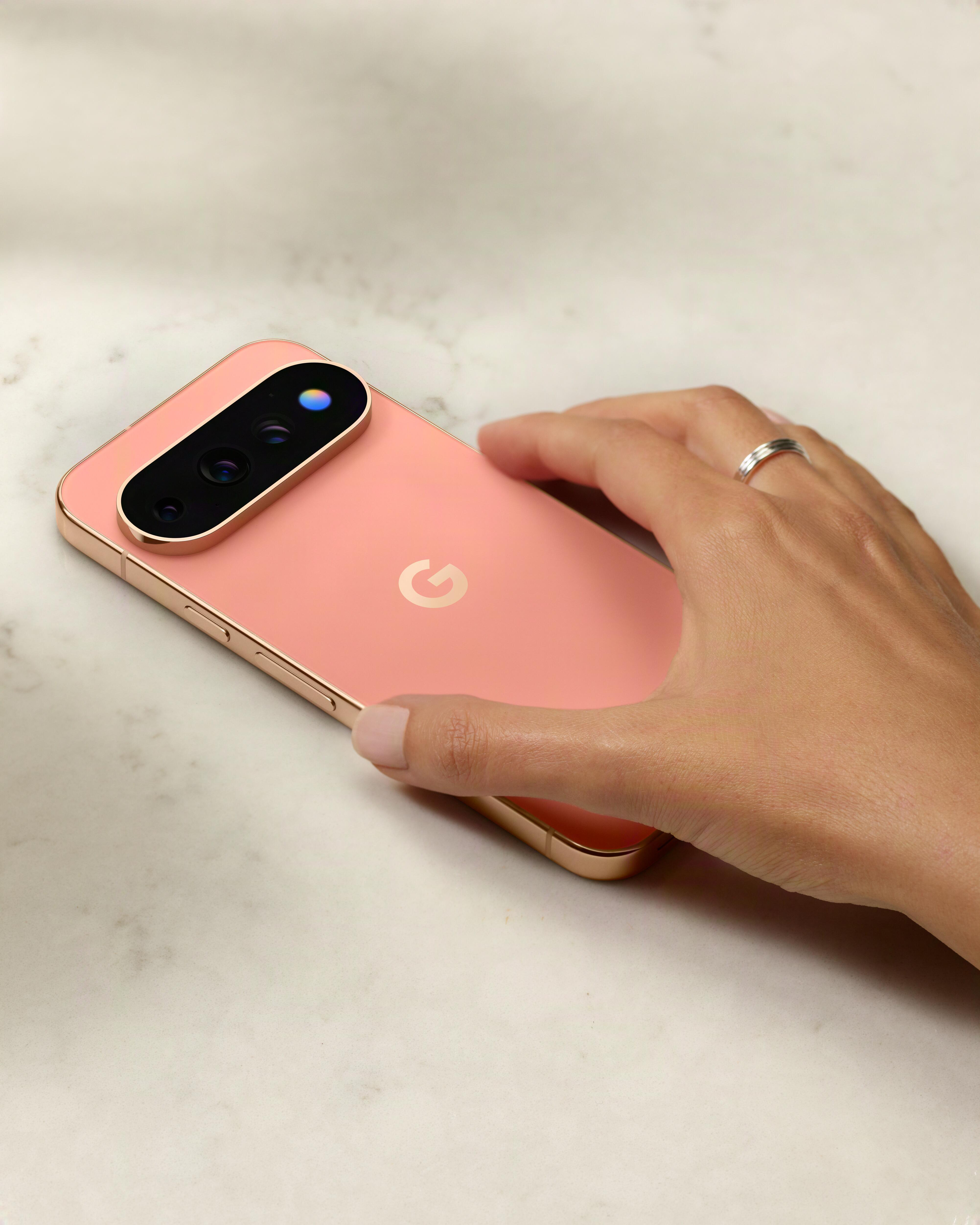 Eine Hand mit Ring liegt auf einem rosa Google Pixel Smartphone auf weißer Marmoroberfläche.