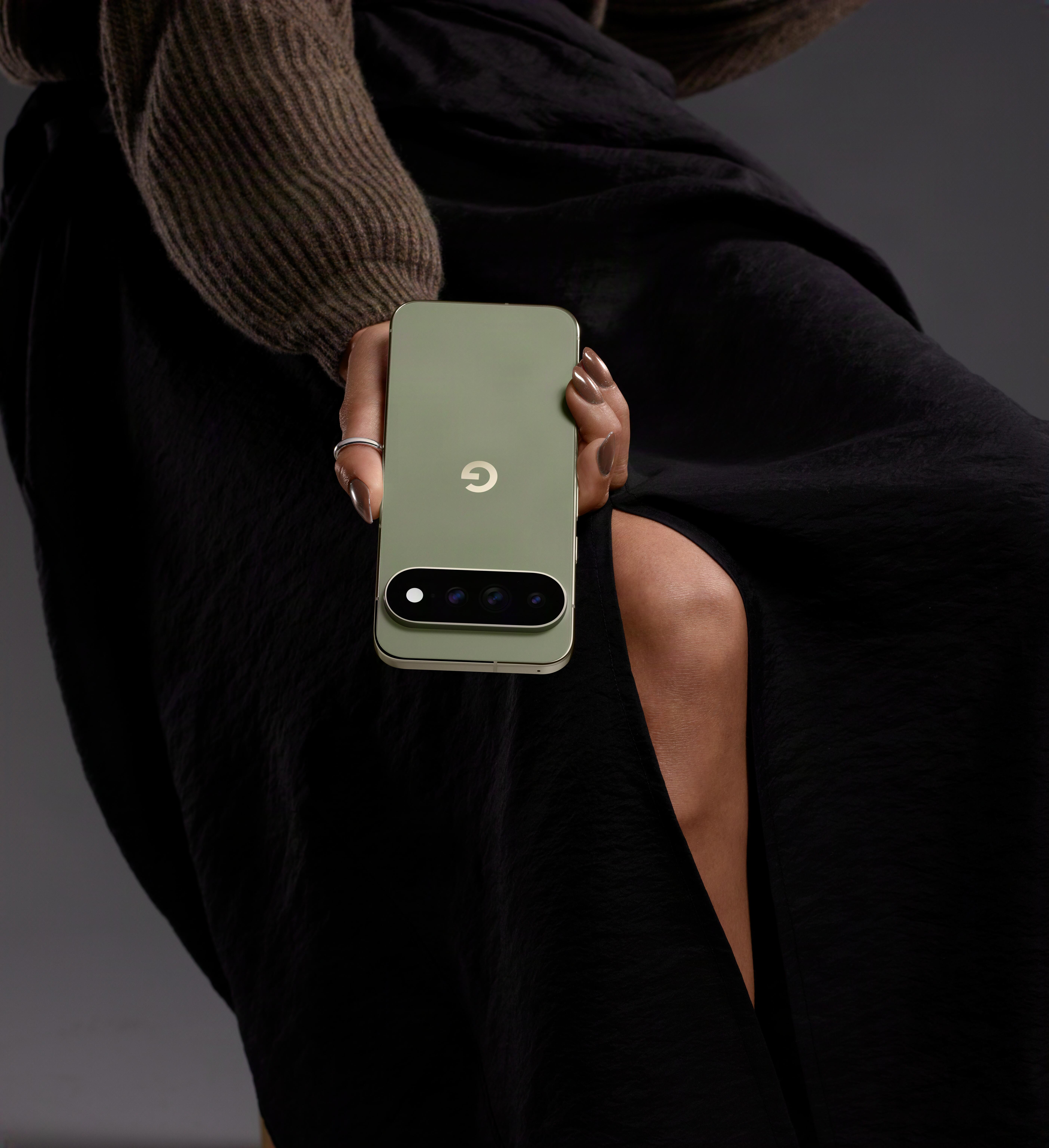 Eine Person im Strickpullover und schwarzen Rock hält ein hellgrünes Smartphone mit Kamera.
