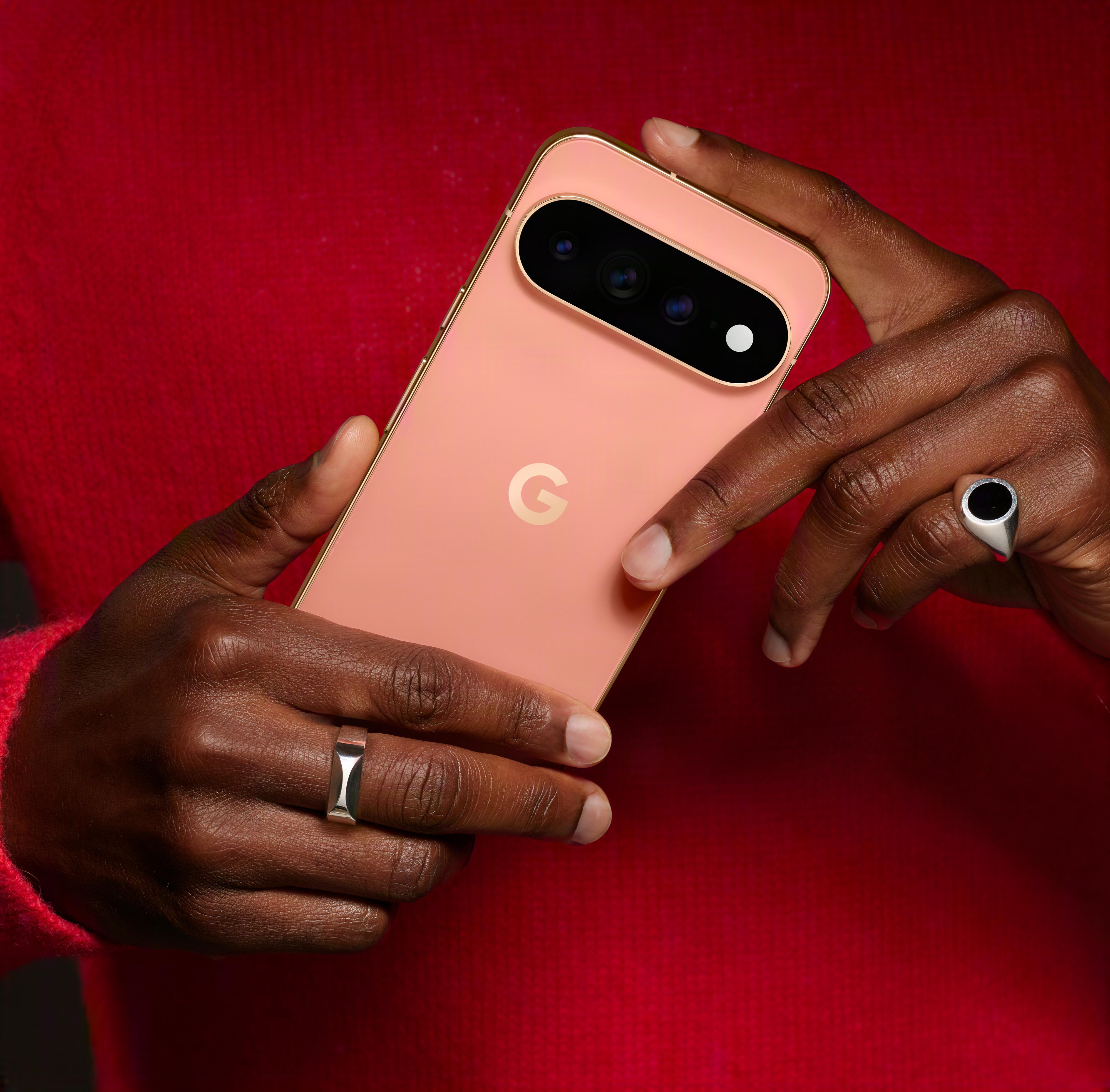 Hände halten ein rosa Smartphone mit dreifacher Kameraleiste vor rotem Hintergrund.