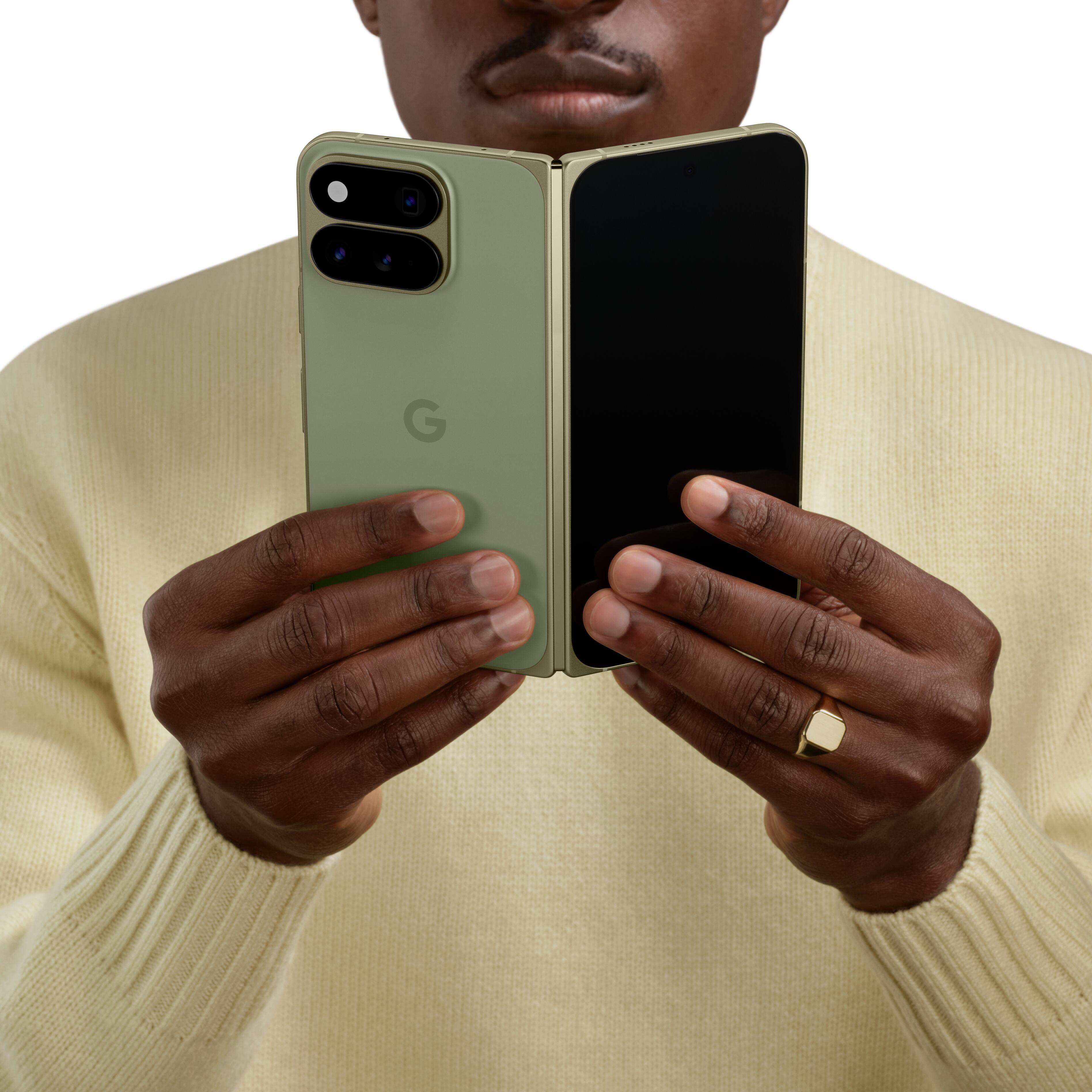 Eine Person in einem Beigepullover hält ein geöffnetes, hellgrünes Faltsmartphone mit Dual-Kamera.