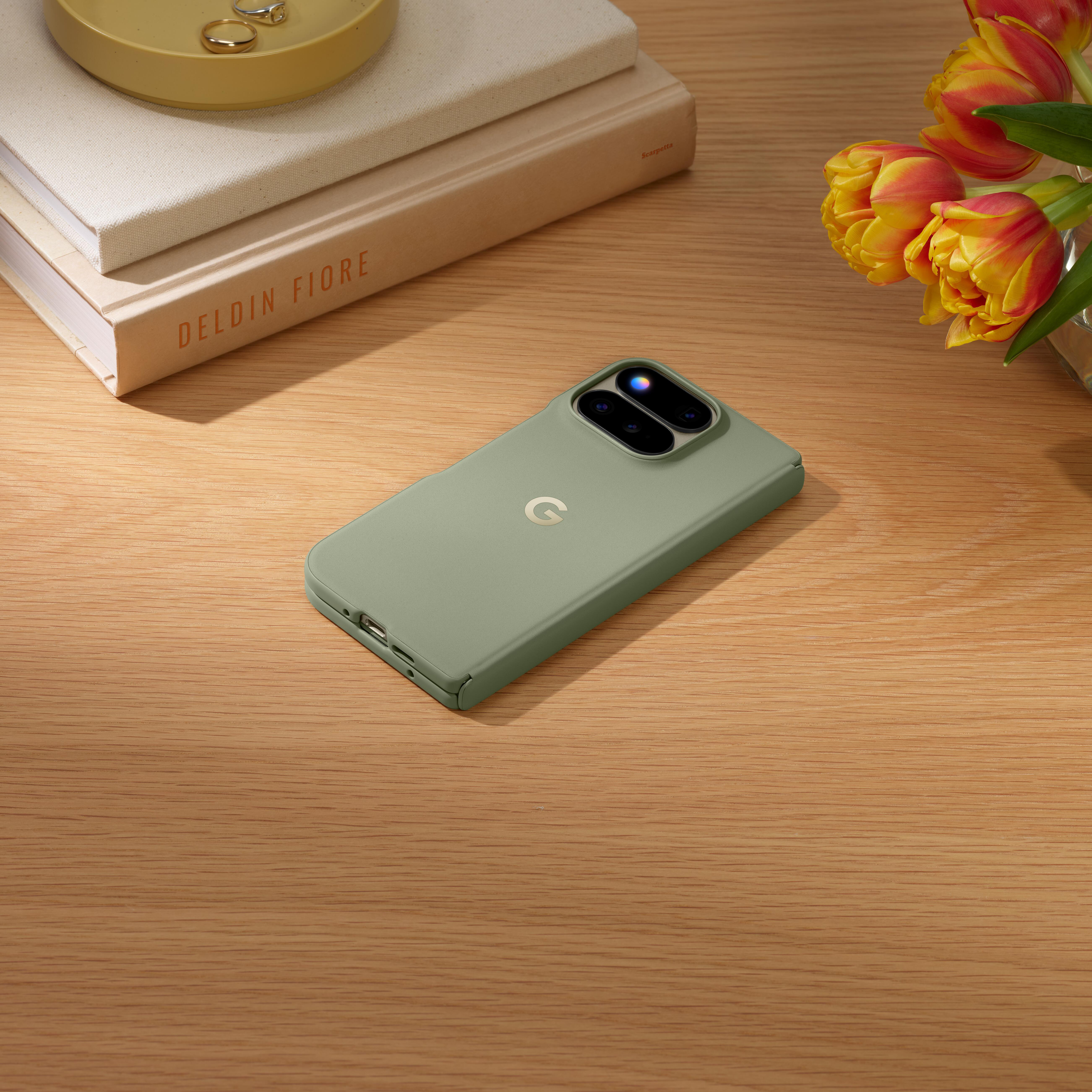 Ein grünes Smartphone liegt auf einem Holztisch neben gestapelten Büchern und gelben Tulpen.