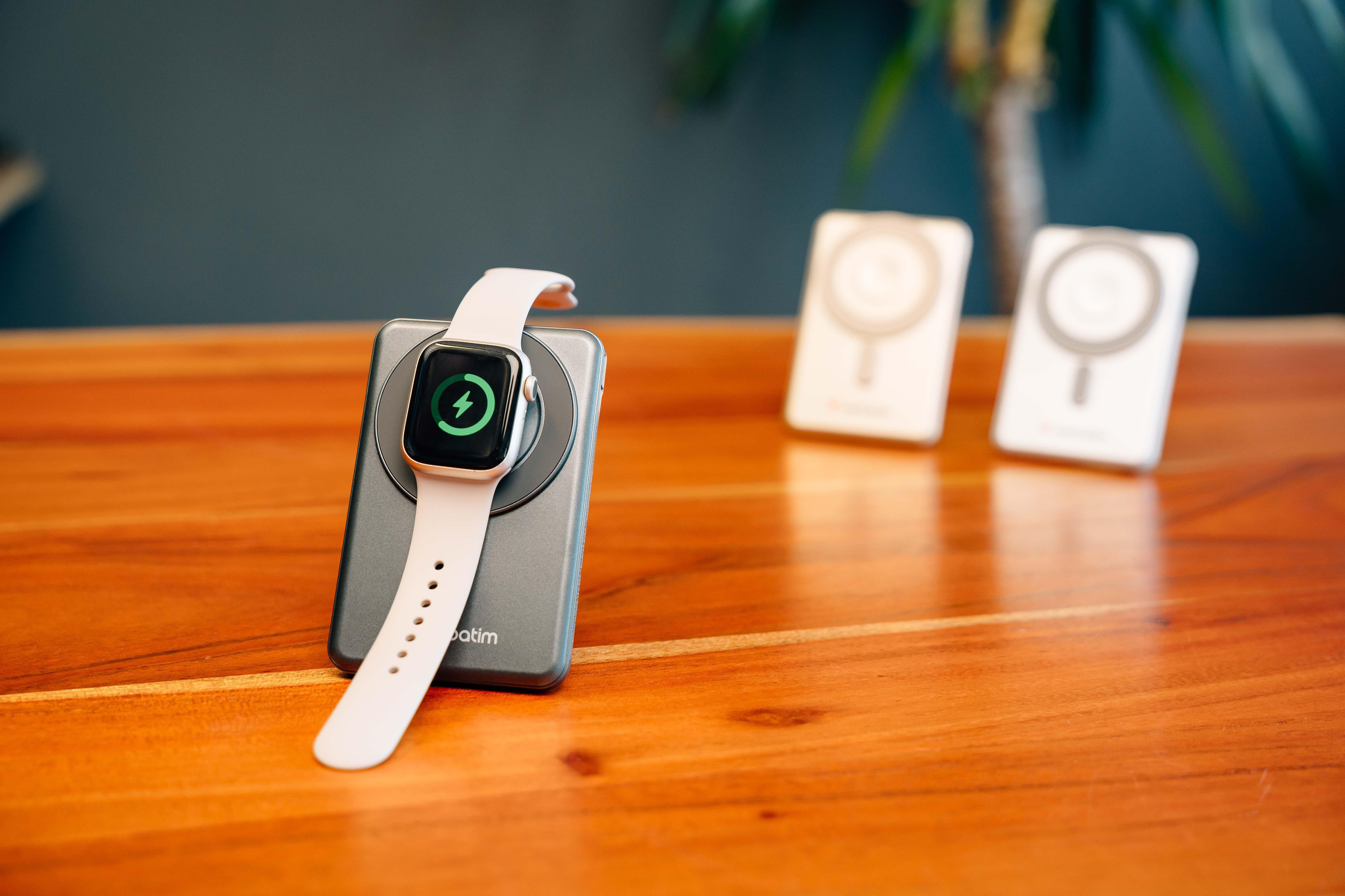 Eine Smartwatch mit weißem Armband lädt auf einem grauen Ständer auf einem Holztisch.
