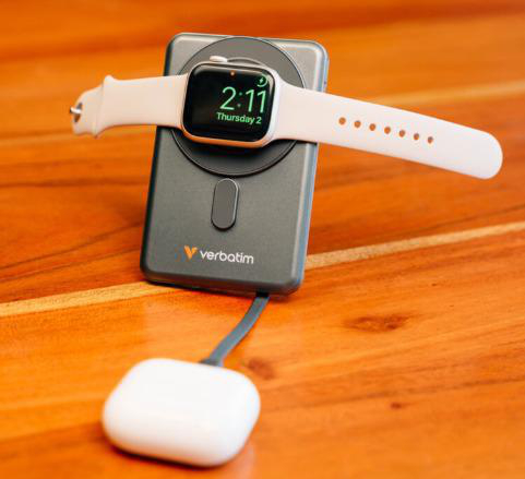 Eine Apple Watch mit weißem Armband liegt auf einer vertikalen Ladestation auf einem Holztisch.