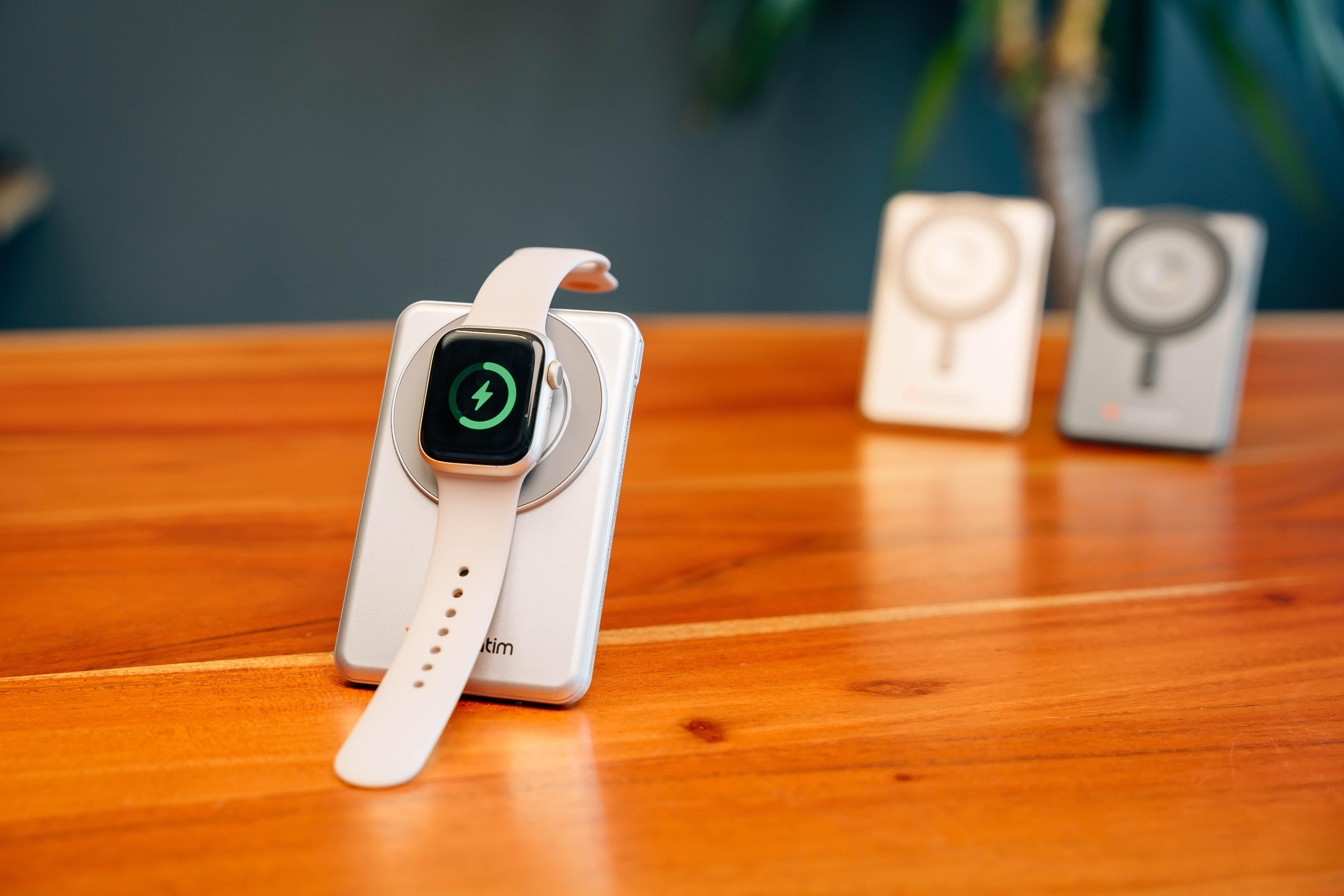 Eine weiße Smartwatch lädt auf einem silbernen Ständer auf einem Holz Tisch.