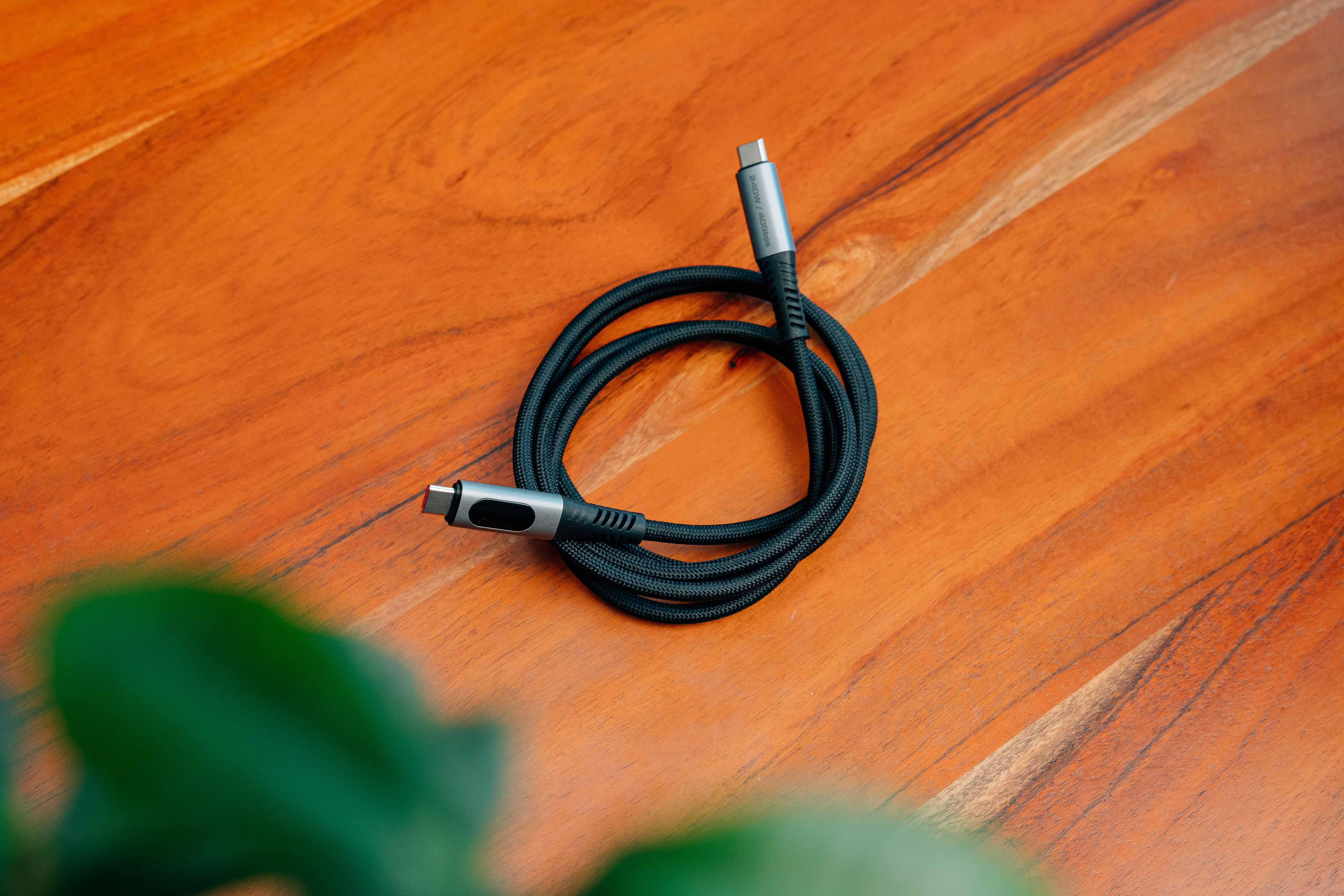 Ein zusammengerolltes schwarzes USB-C-Kabel mit grauen Steckern liegt auf einer Holztischplatte.