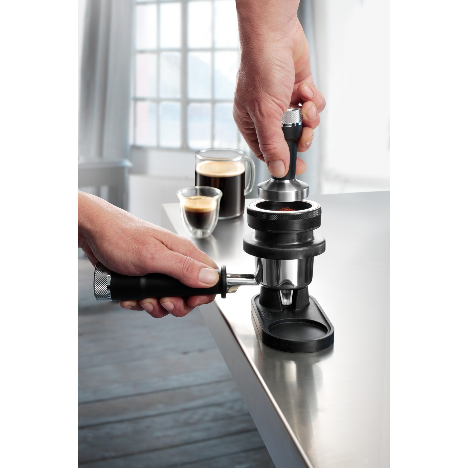 Une main presse le café moulu avec un tamper tandis que l'autre tient le porte-filtre.