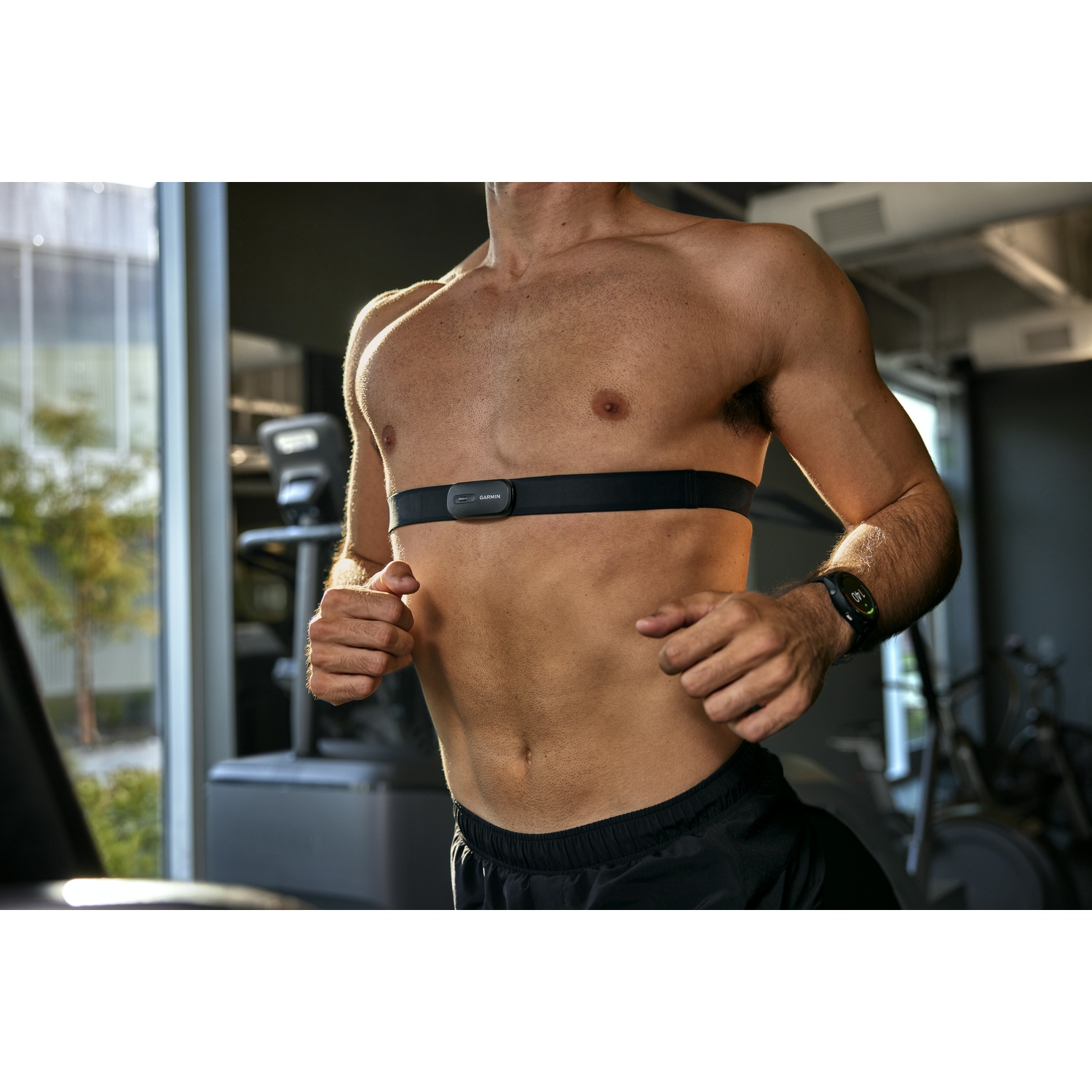 Un homme torse nu court sur un tapis de course avec une ceinture cardio noire.