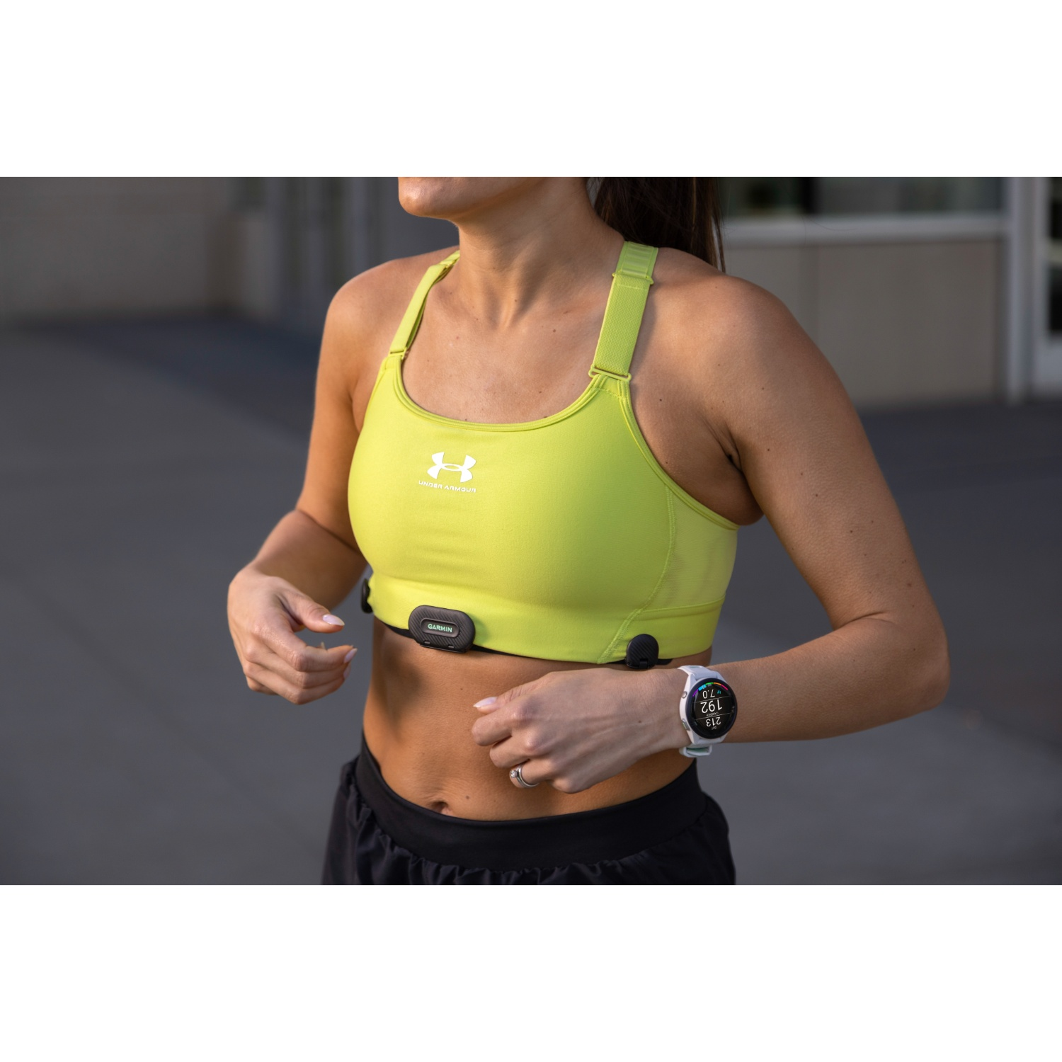 Een vrouw in een gele sportbeha en zwarte shorts draagt een Garmin hartslagmeter en sporthorloge.