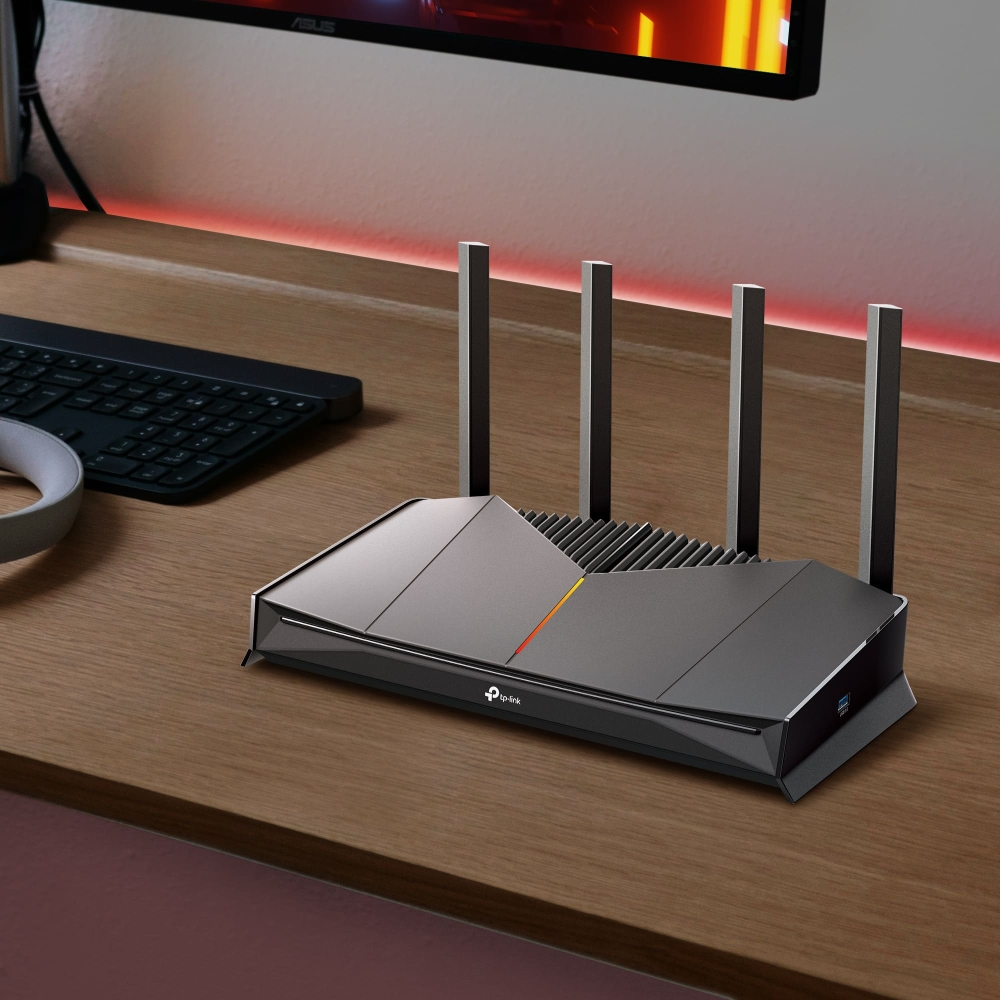 Dört antenli gri bir TP-Link yönlendirici, klavyenin yanında ahşap bir masada duruyor.