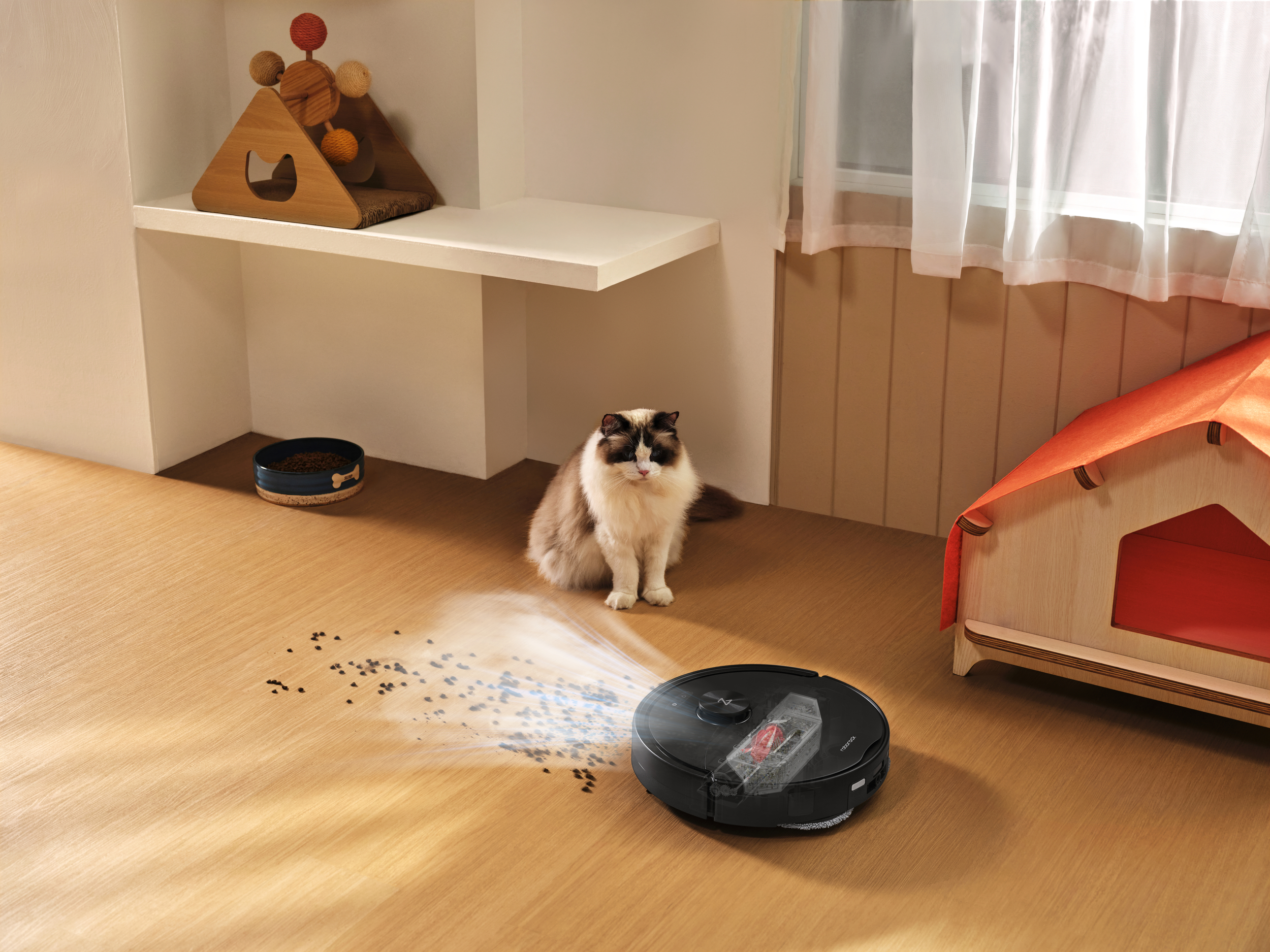 Ein Saugroboter reinigt verschüttetes Futter von einem Holzboden, während eine Katze zusieht.