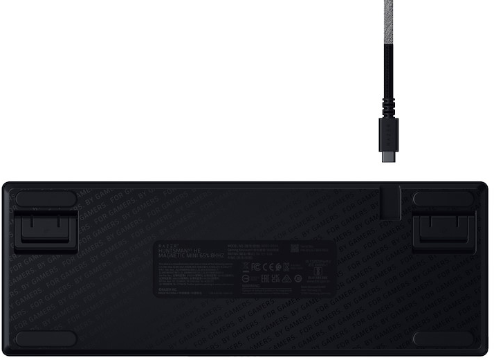 Lato inferiore di una tastiera nera con piedini pieghevoli e un cavo USB mostrato sopra.