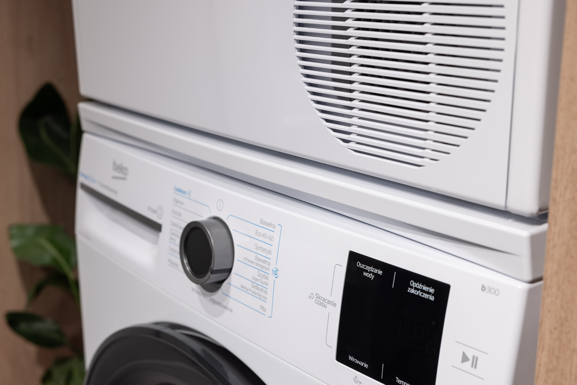 Biała suszarka do ubrań stoi na białej pralce marki Beko w pomieszczeniu.