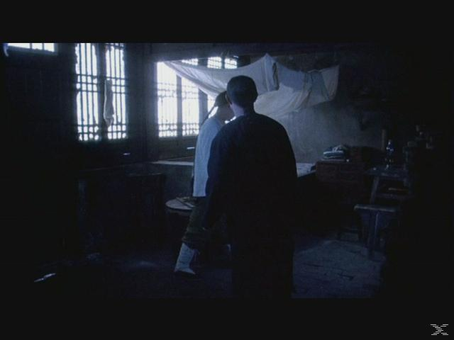 Zwei Personen stehen in einem schwach beleuchteten Raum mit Gitterfenstern und Stoff an der Decke.