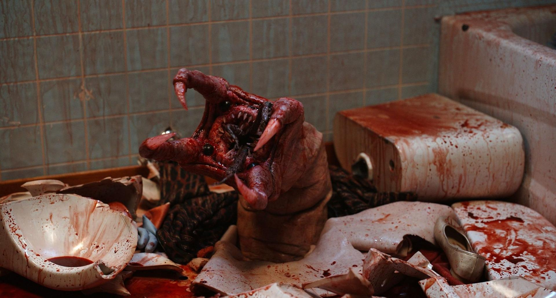 Ein blutiges, wurmähnliches Monster mit scharfen Klauen ragt in einem blutverschmierten Badezimmer empor.