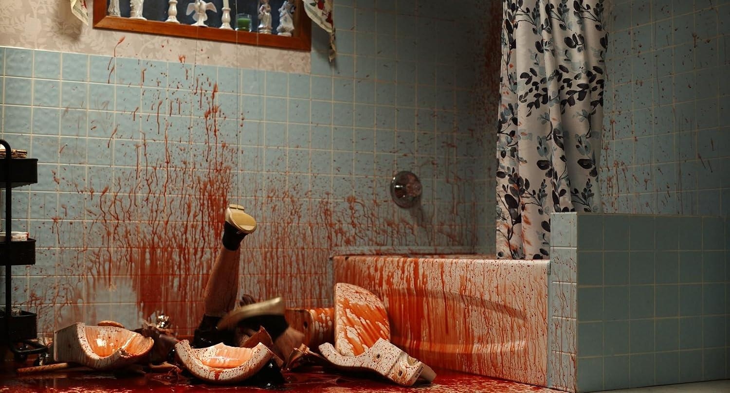 Badezimmer voller Blutspuren, mit zerbrochenen Keramikgegenständen am Boden und Beinen, die aus der Wanne ragen.