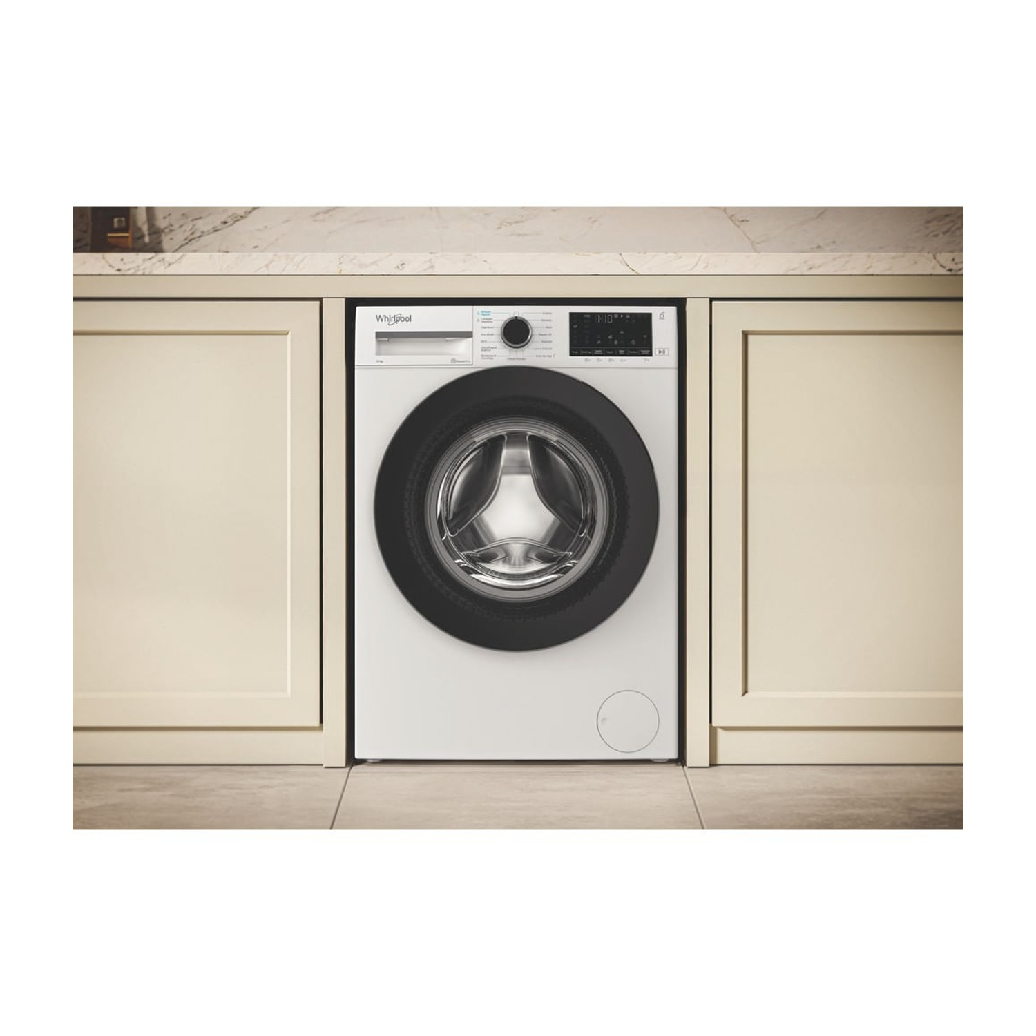 Una lavatrice bianca Whirlpool è posizionata tra mobili da cucina beige sotto un piano in marmo.