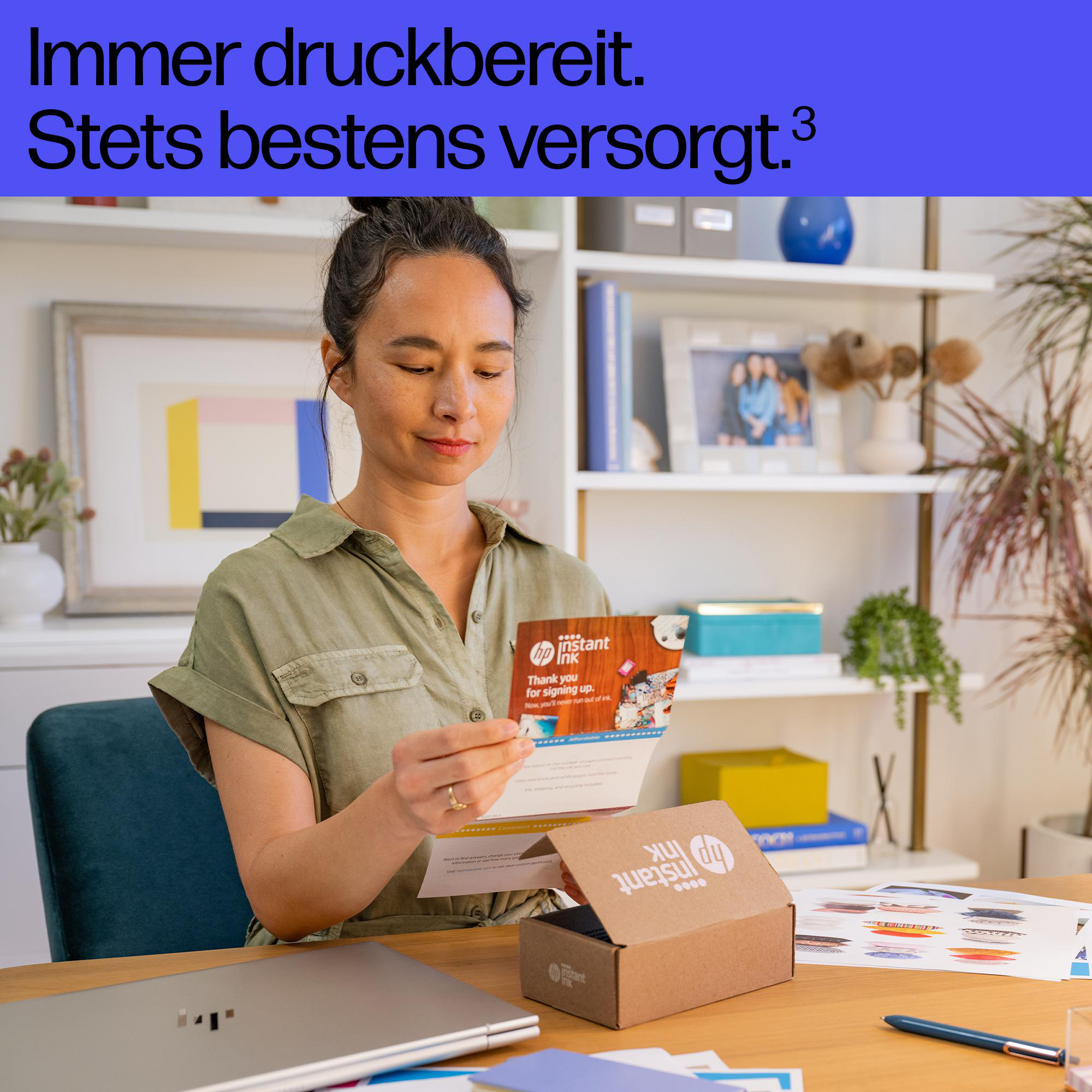 Eine Frau im grünen Hemd liest in einem Raum mit Regalen einen Brief neben einem HP Instant Ink Karton und einem Laptop.