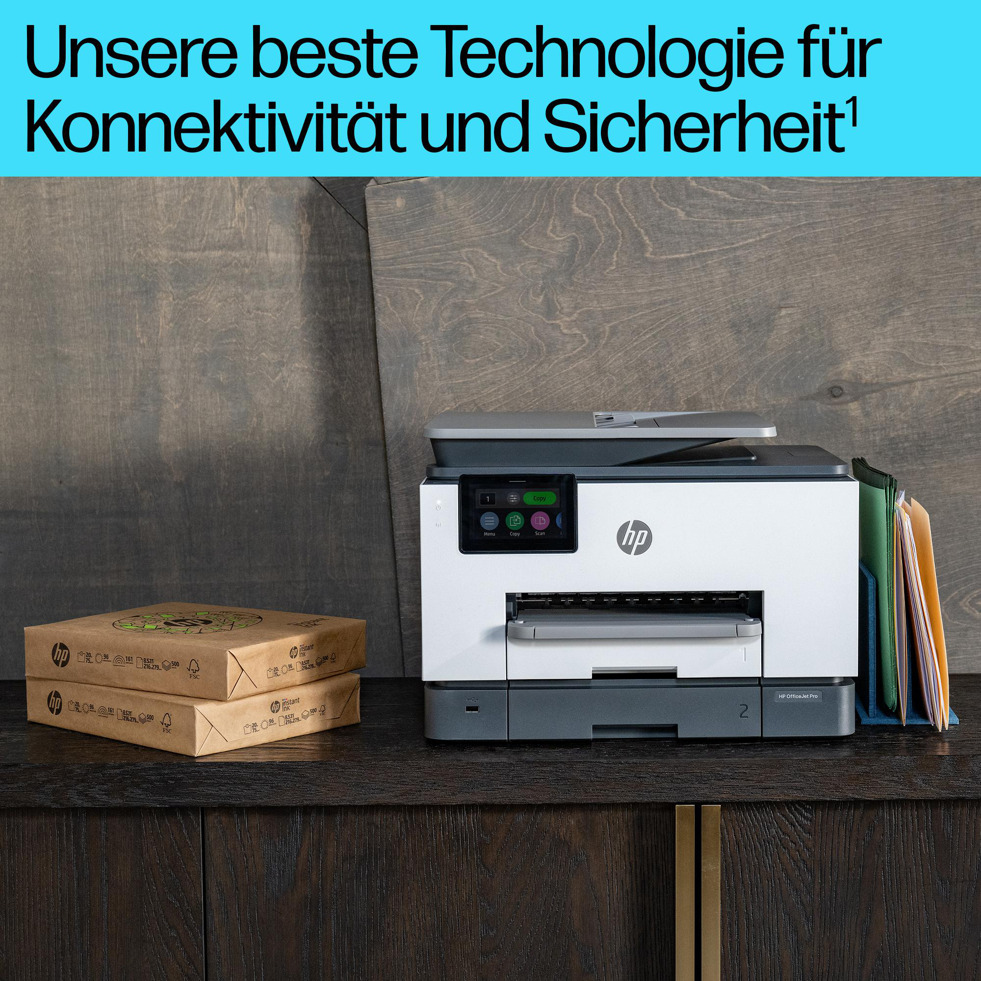 Ein HP OfficeJet Pro Drucker steht auf einem dunklen Holztisch, daneben Papierpakete und Aktenordner.