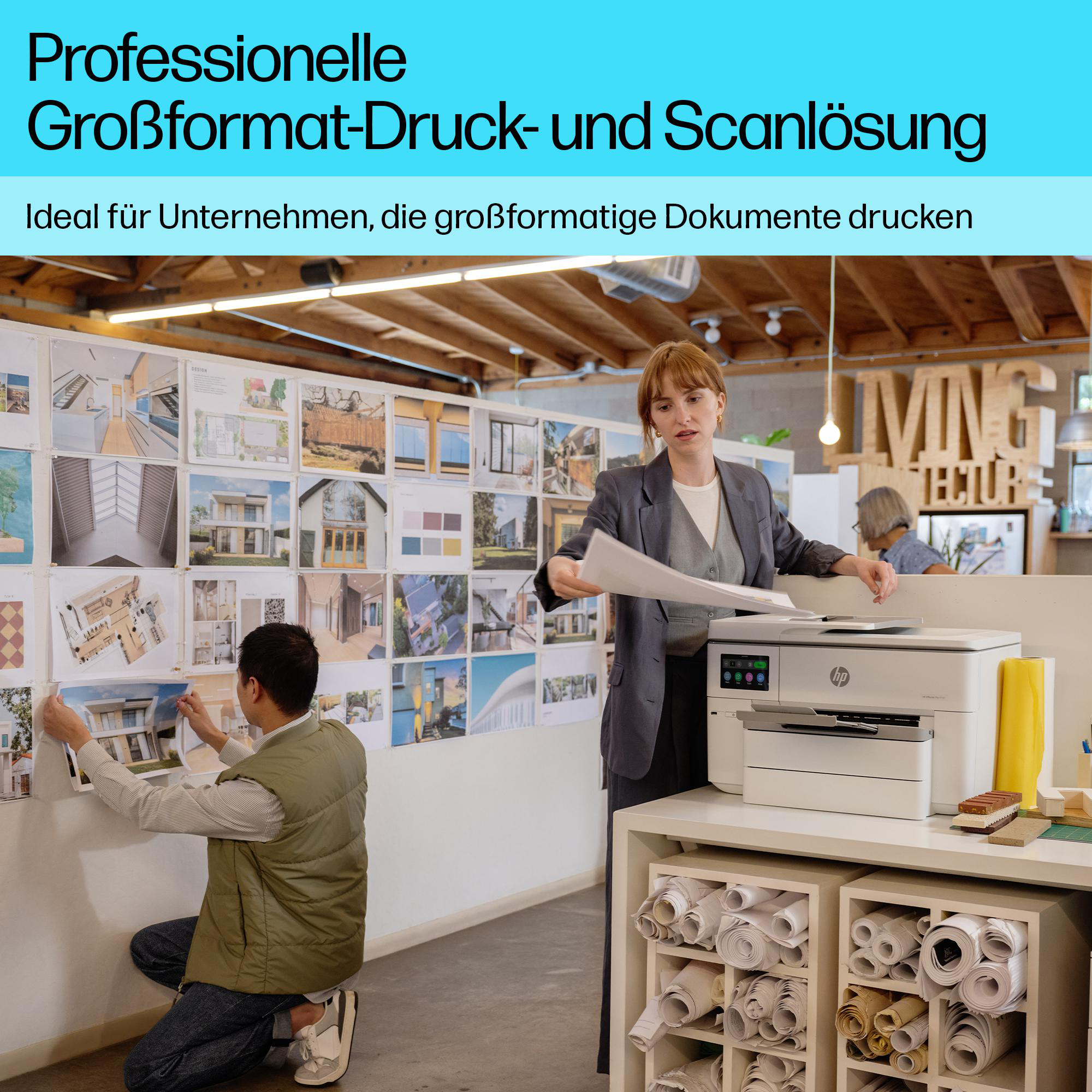 Büro mit zwei Personen, die Architekturpläne drucken und aufhängen, neben einem großen HP-Drucker.