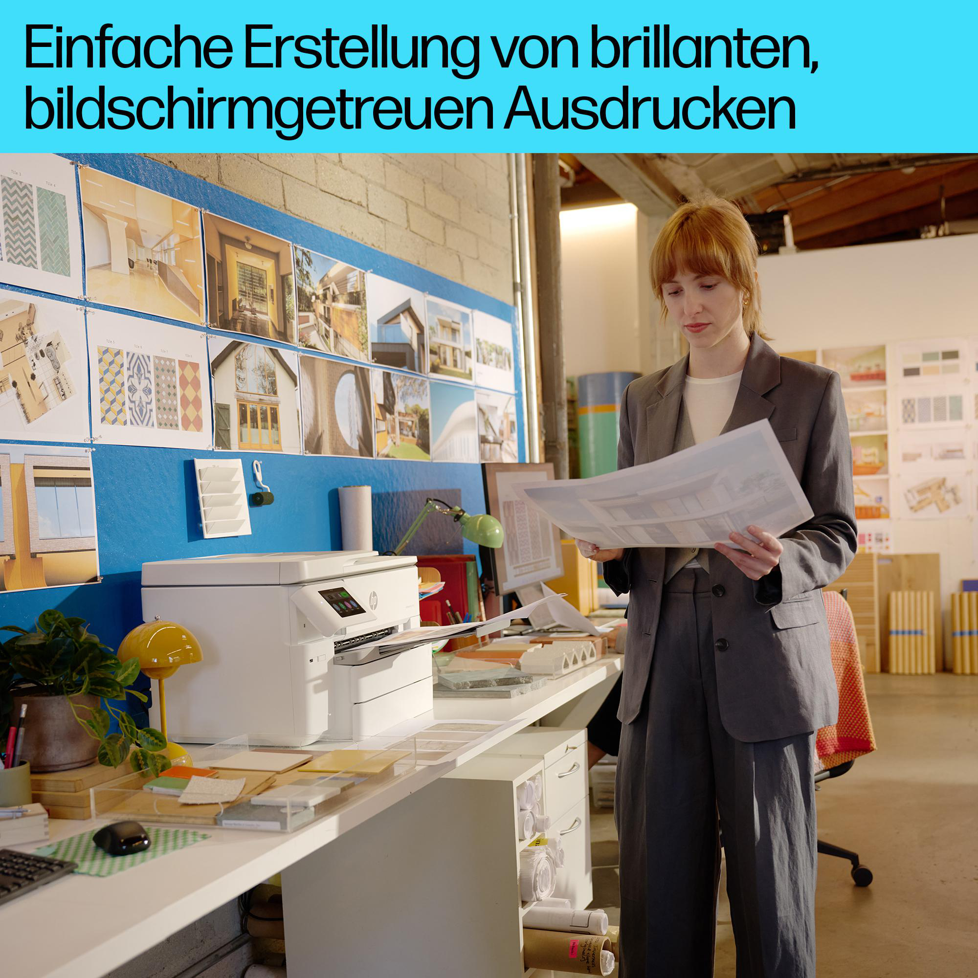 Eine Frau im grauen Anzug prüft Architekturpläne in einem Büro mit Drucker und Designtafeln im Hintergrund.