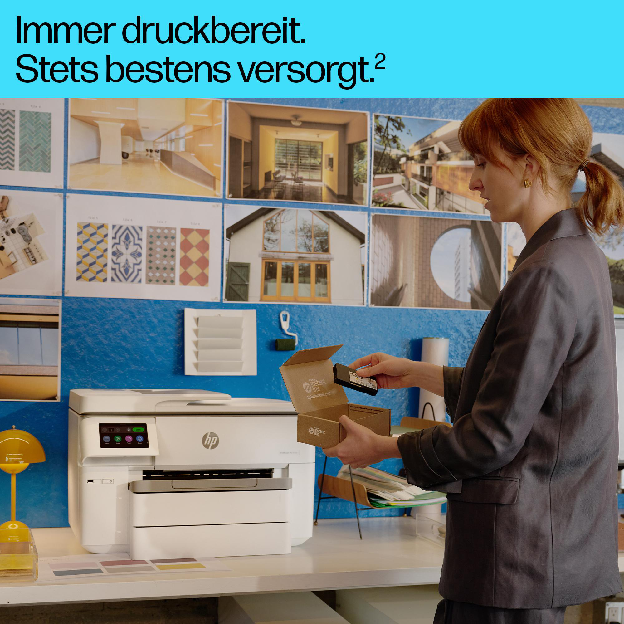 Eine Frau in einem grauen Blazer öffnet ein kleines HP-Paket vor einem weißen Drucker und einer blauen Pinnwand.