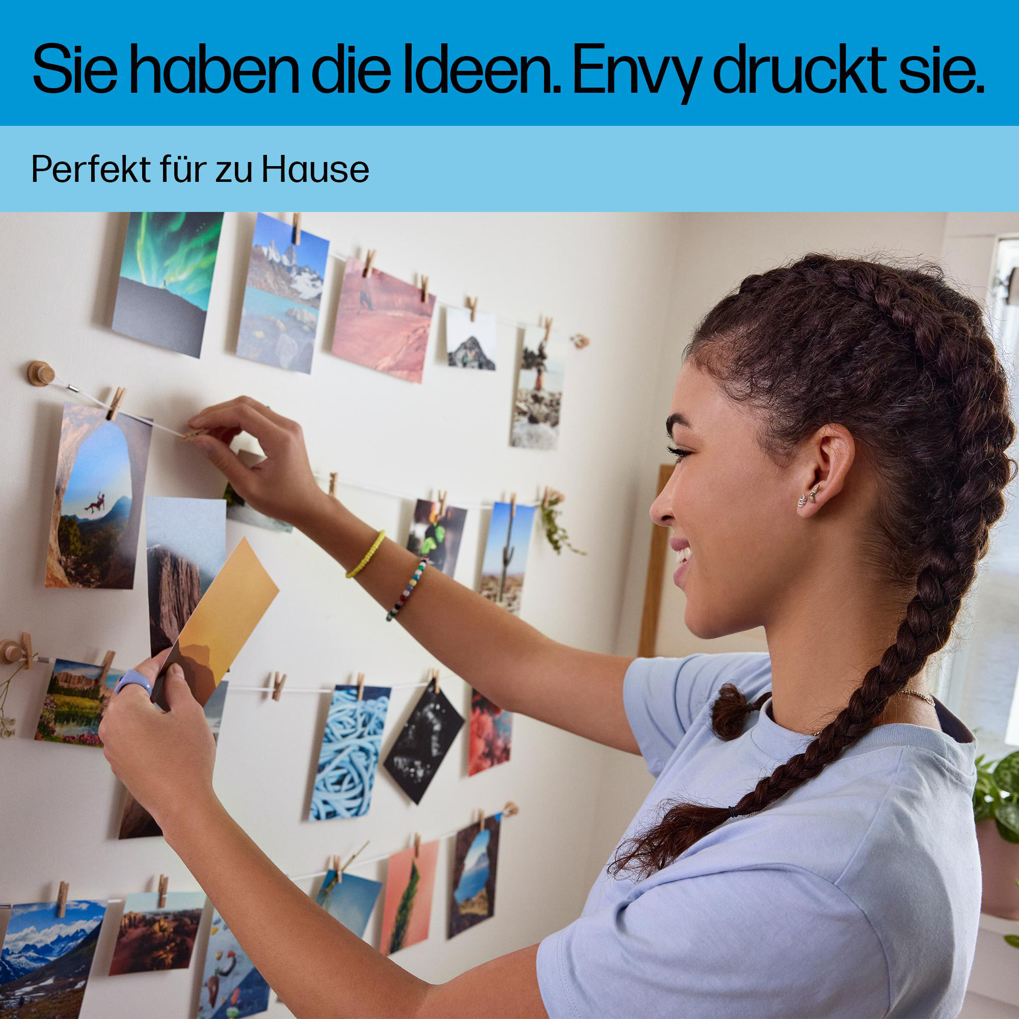 Eine lächelnde junge Frau hängt bunte Fotos an einer Schnur an eine weiße Wand.