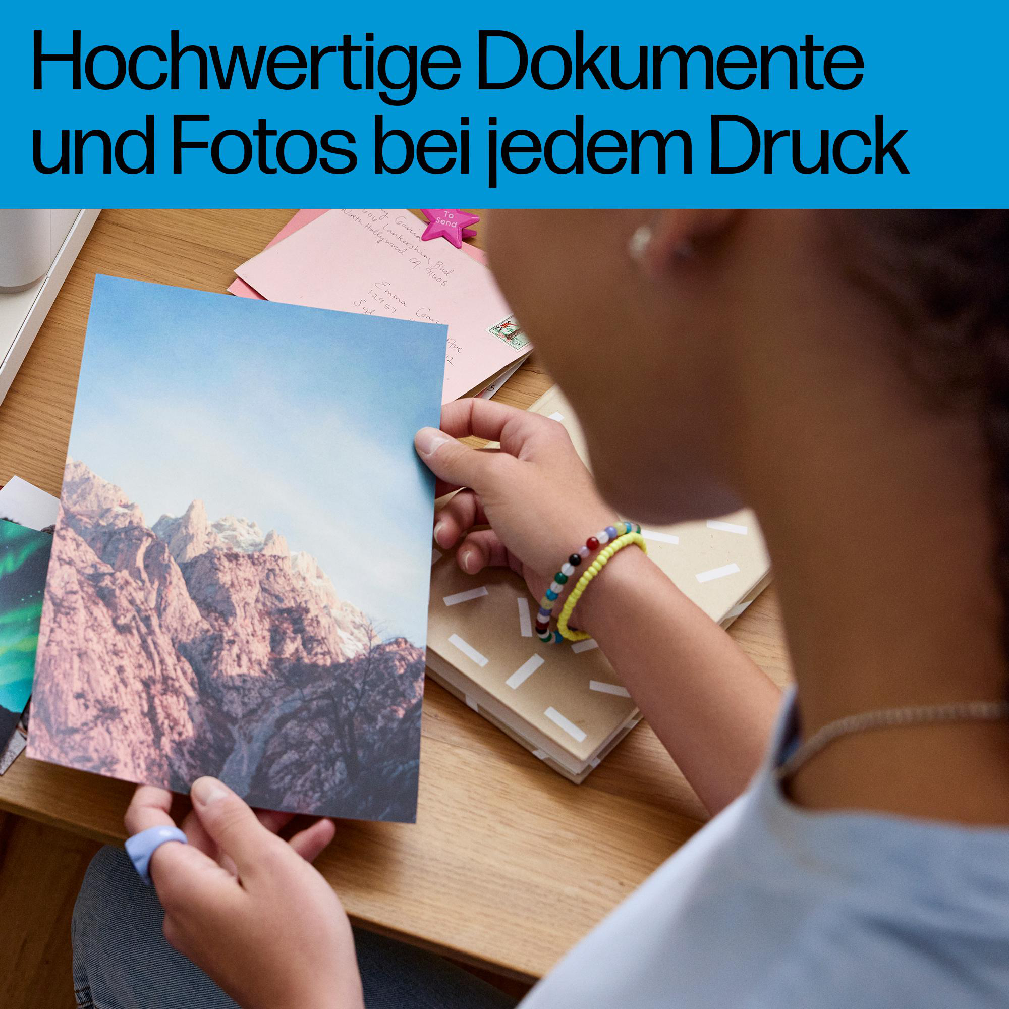 Eine Person hält ein gedrucktes Foto von Bergen in den Händen, auf einem Holztisch.
