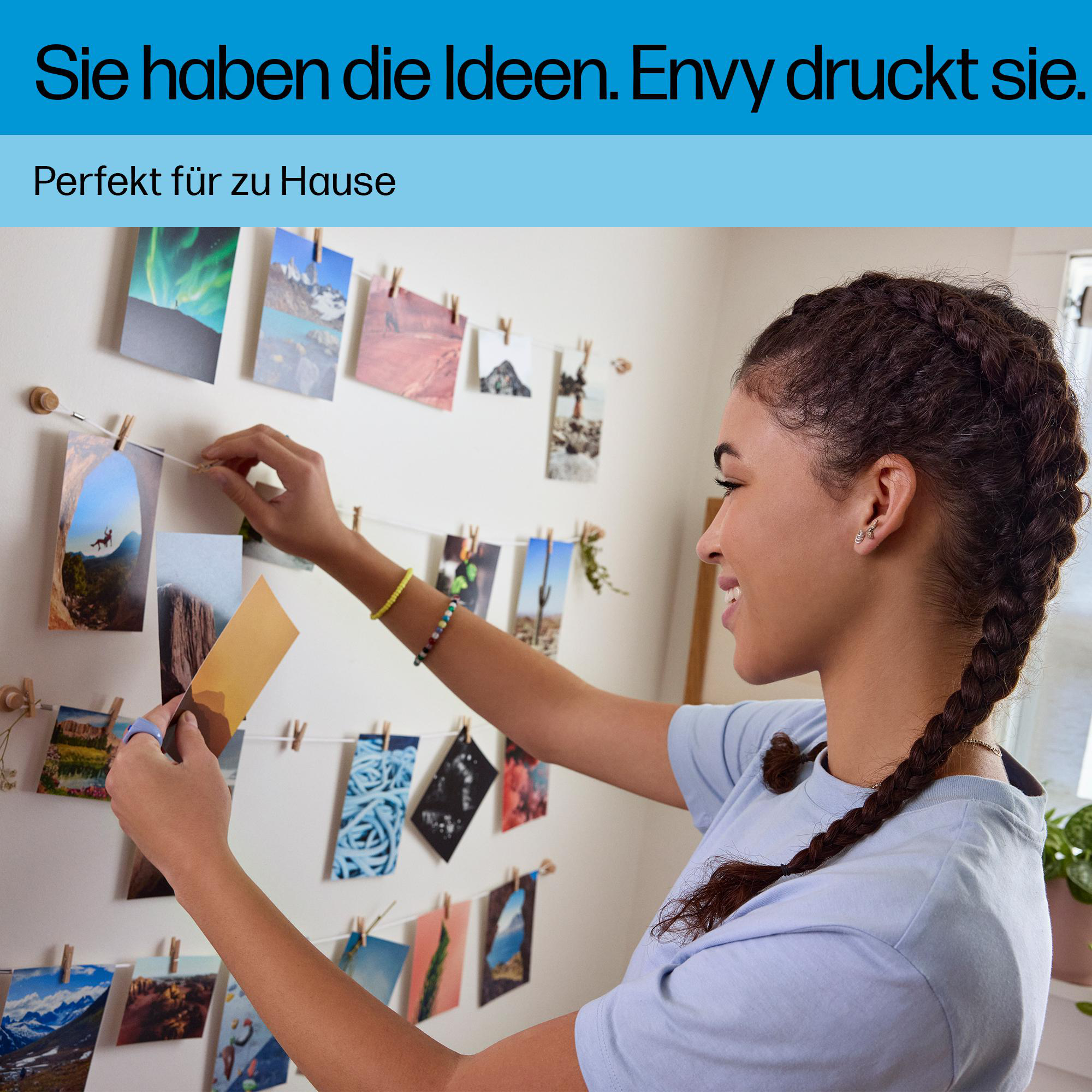 Junge Frau hängt Fotos mit Klammern an eine weiße Wand.