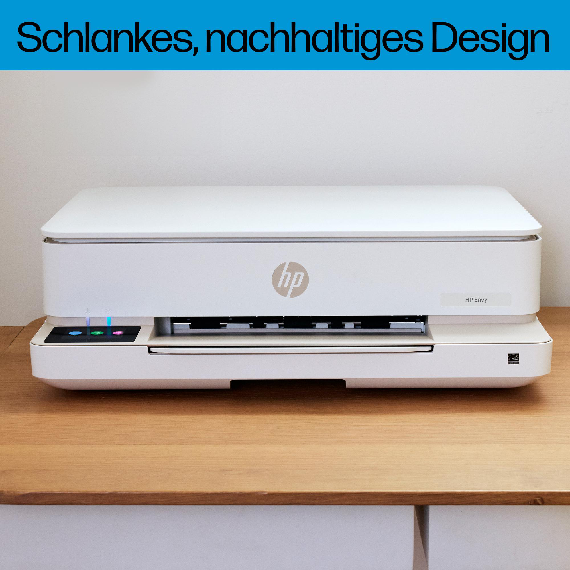 Ein weißer HP Envy Drucker steht auf einem Holzschreibtisch vor einer weißen Wand.